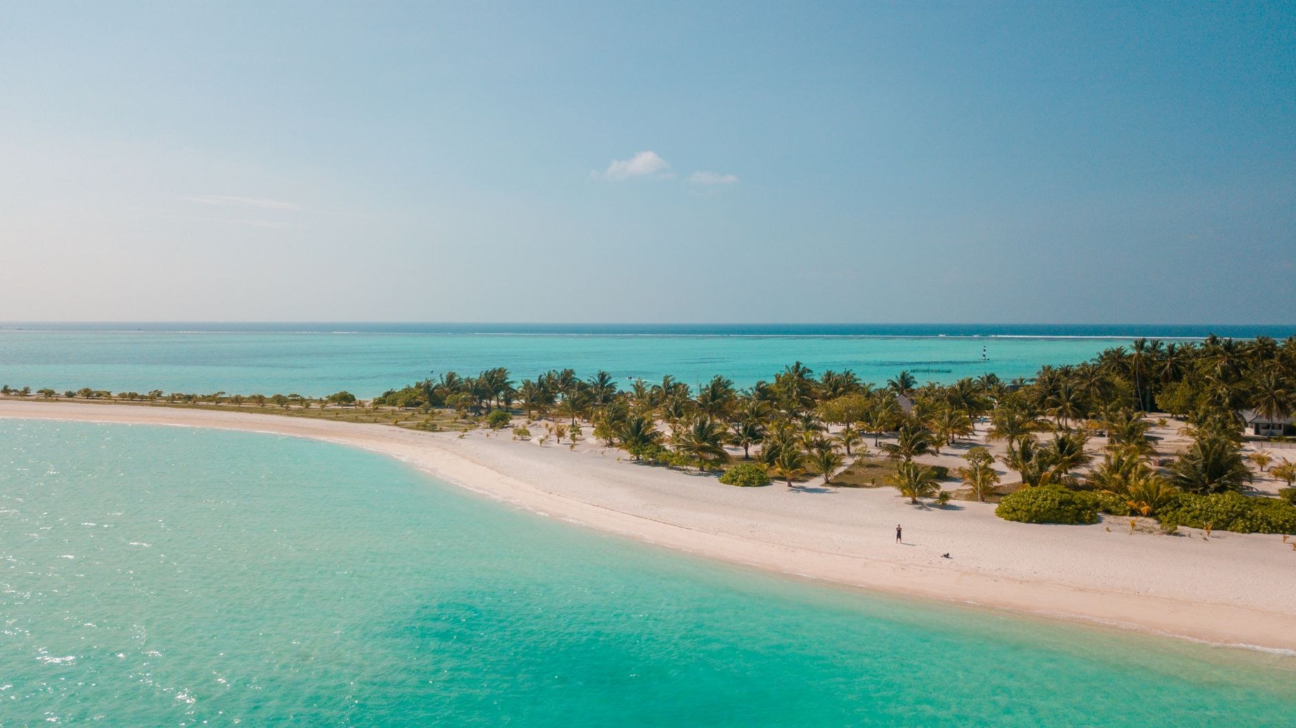 A curving white sandbank tapering into turquoise waters surrounded by green coconut palm trees