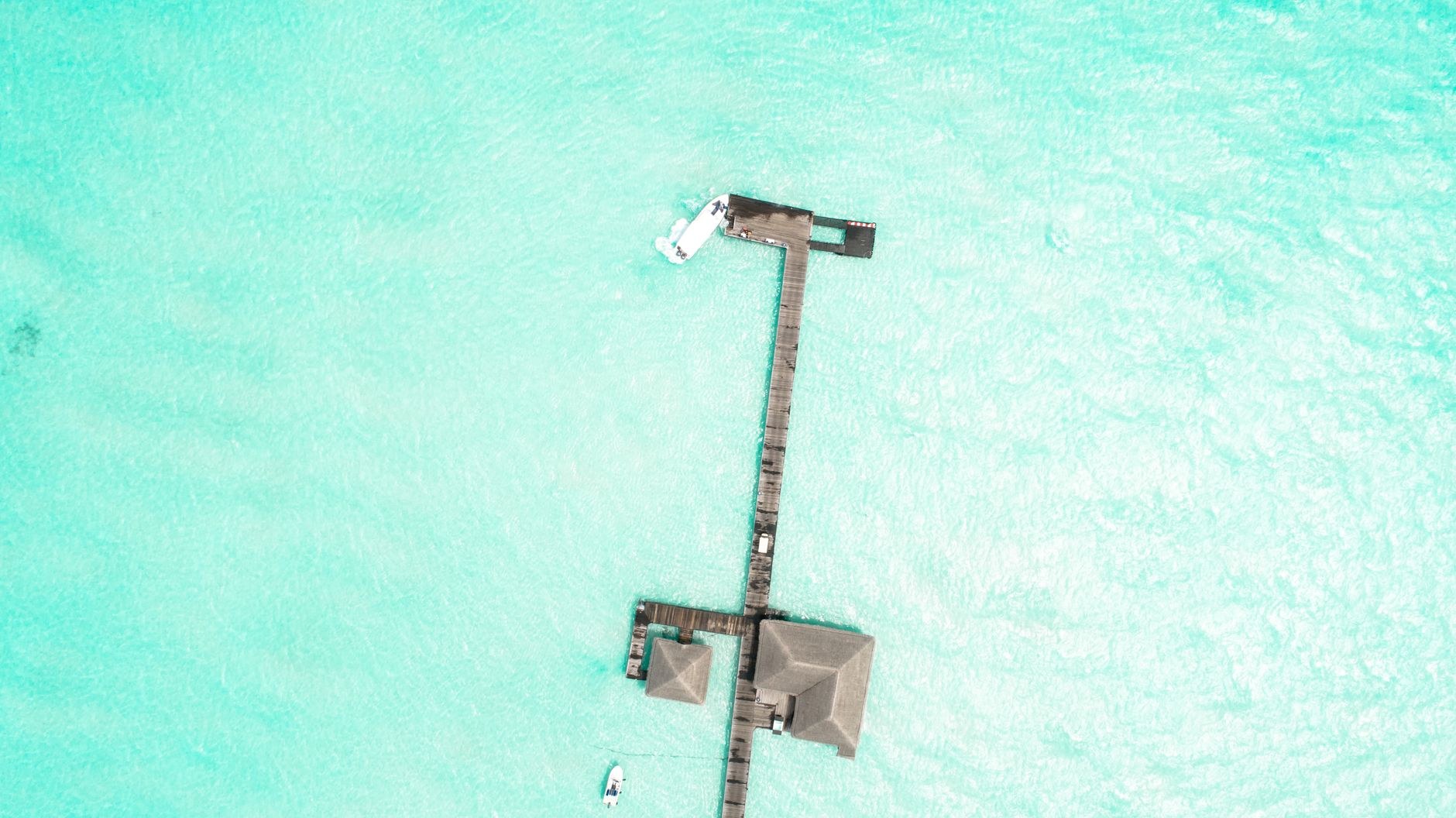 Thatched-roof luxury overwater bungalows on wooden stilts extending over a calm crystalline turquoise lagoon