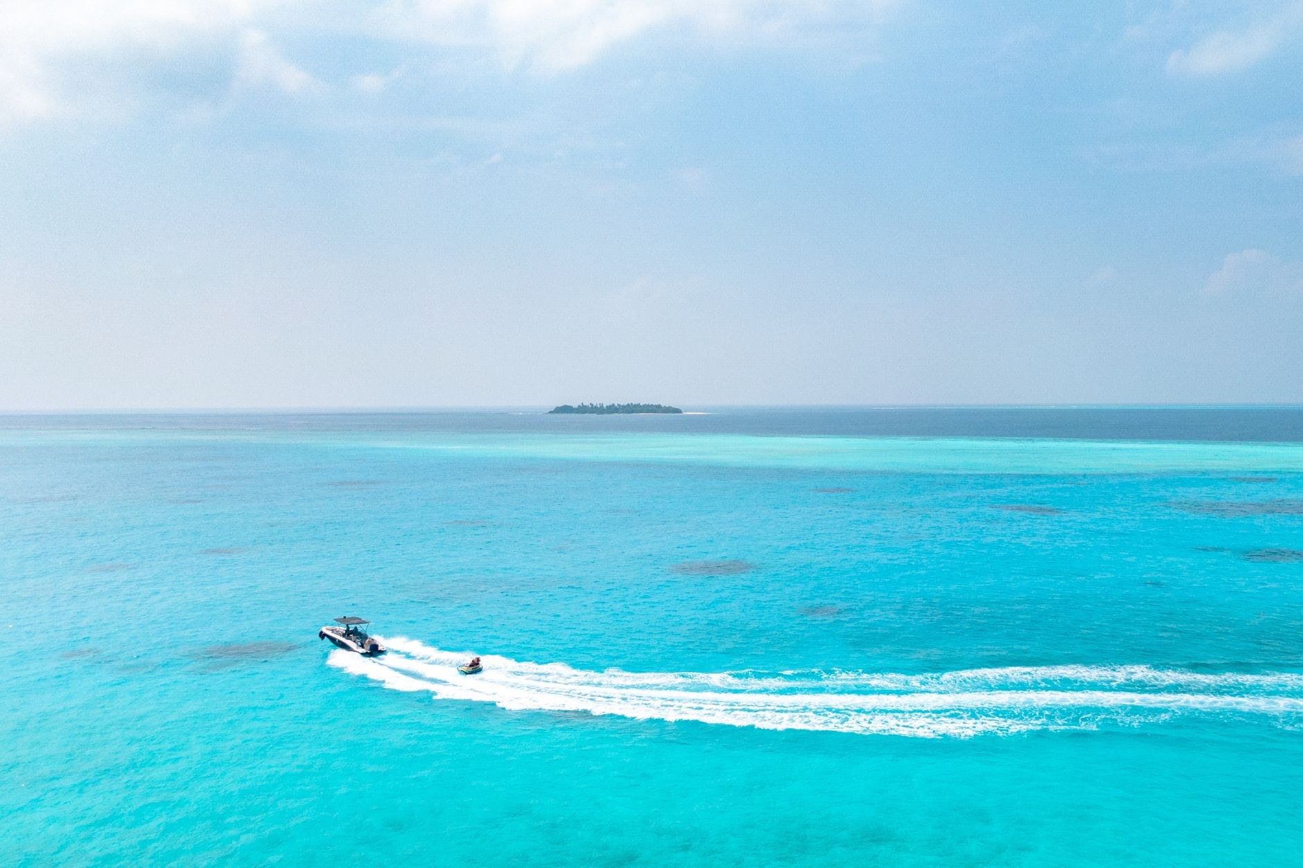 A sleek twin-engine passenger speedboat slicing across deep blue ocean waters leaving a white foamy wake