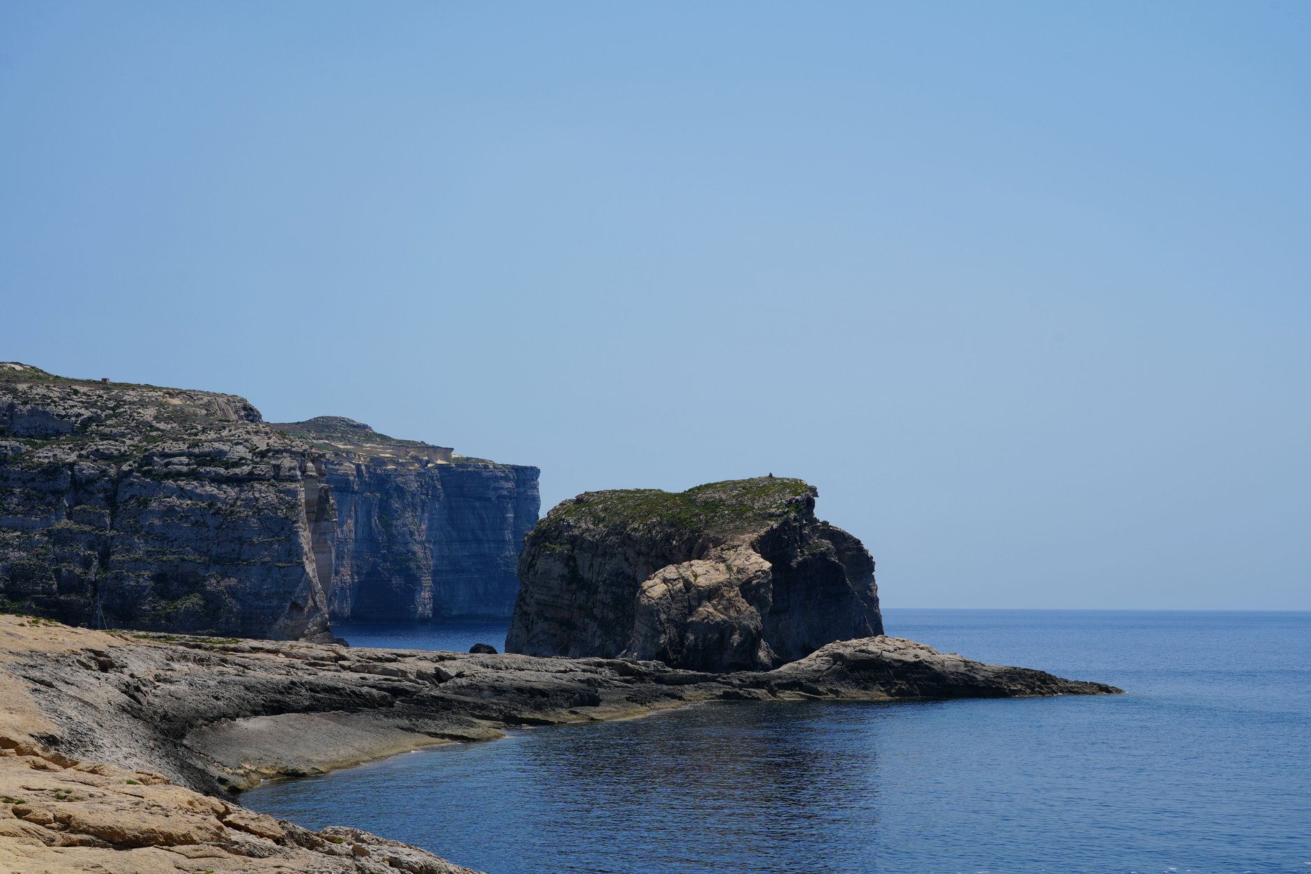 Rugged limestone coastal cliffs and deep blue water around Dwejra Bay on the western coast of Gozo