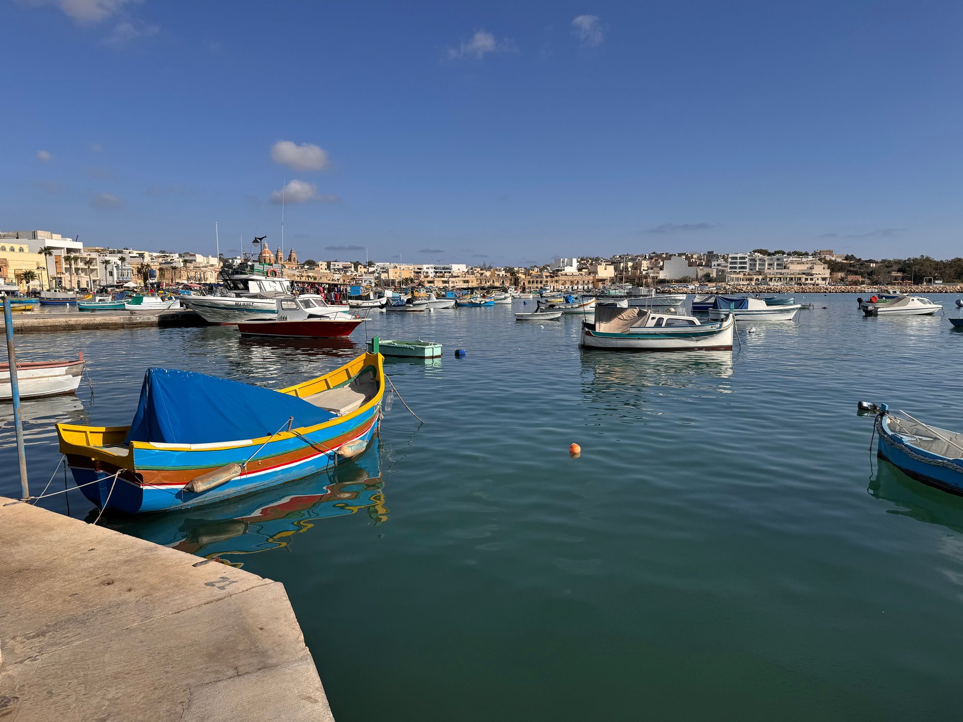 Traditional brightly painted wooden luzzu fishing boats moored in the calm turquoise waters of Marsaxlokk harbor