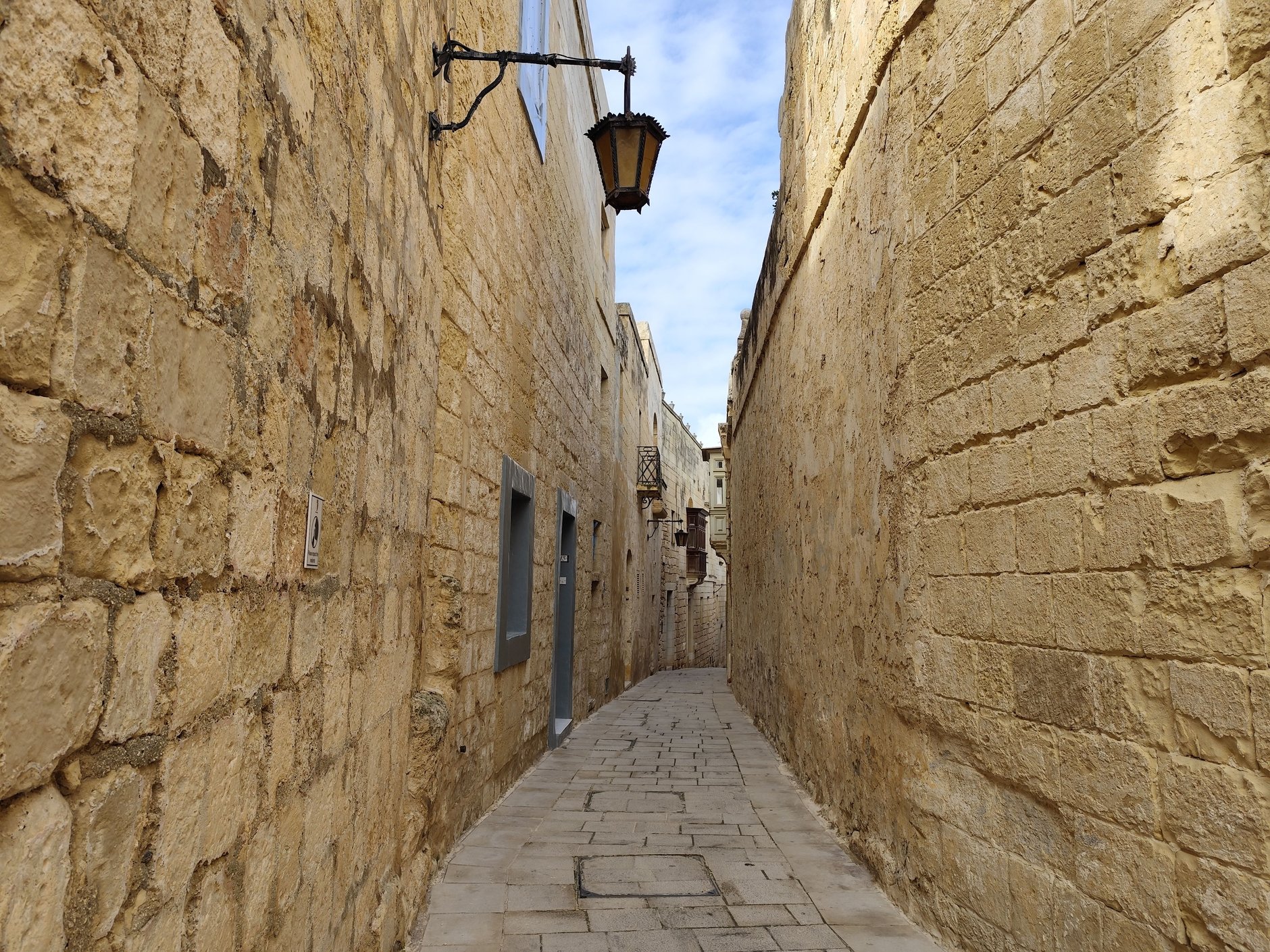 Quiet narrow sandstone alley with colorful wooden Maltese balconies and lantern lights in the medieval walled city of Mdina