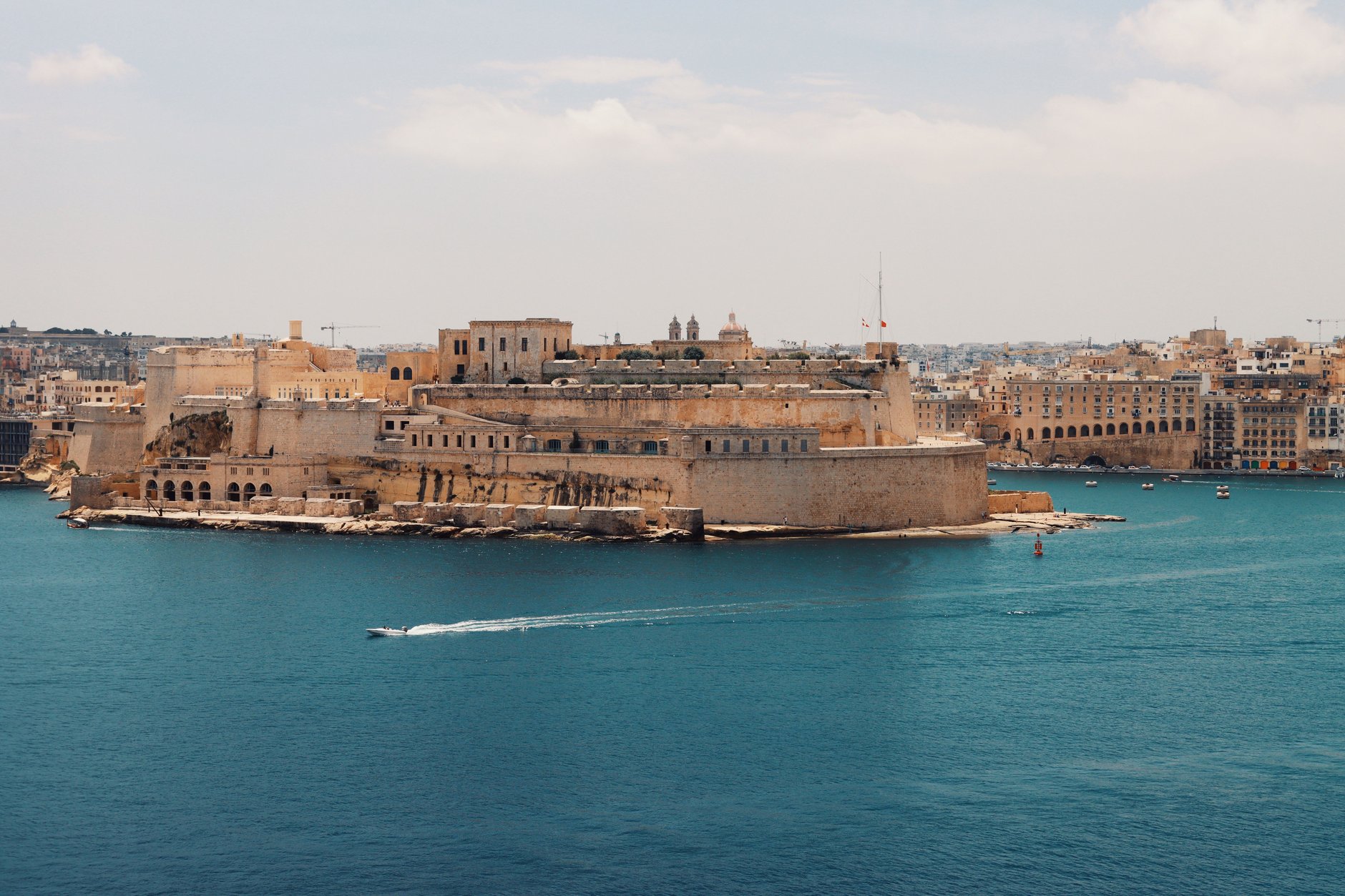 Historic stone ramparts of Fort St Angelo rising above the waterfront promenade and yacht marina in Birgu