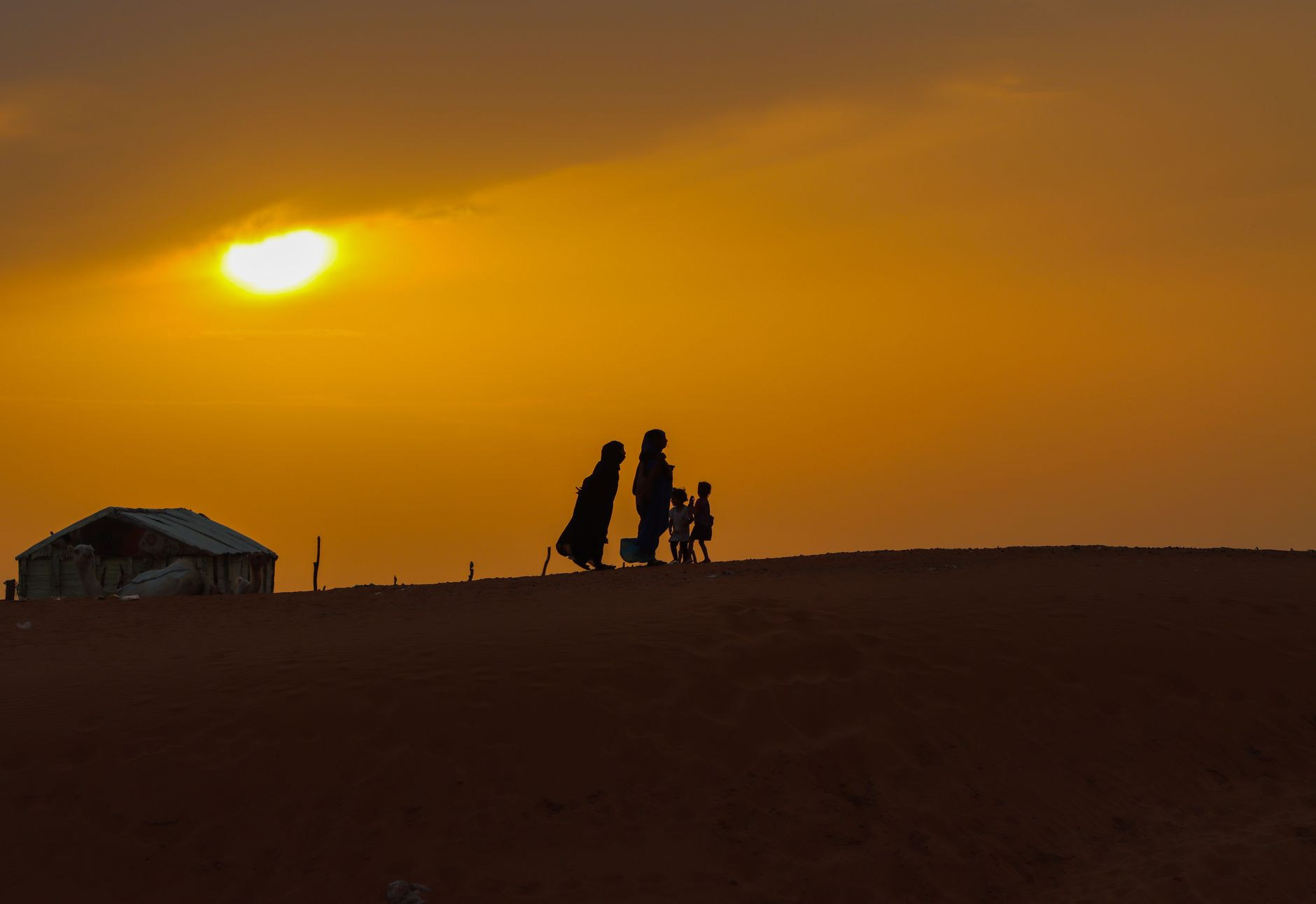 Silhouettes of local residents walking along the crest of a desert sand dune at sunset near Nouakchott