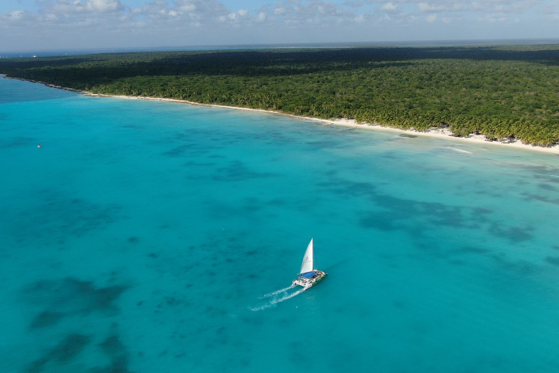 White sailing catamaran anchored in crystal-clear turquoise waters beside an idyllic tropical white-sand beach
