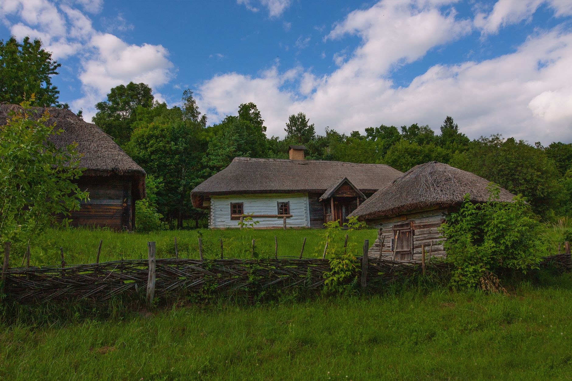 A traditional Moldovan rural cottage with ornate blue-painted trim and thatched woven wicker fence