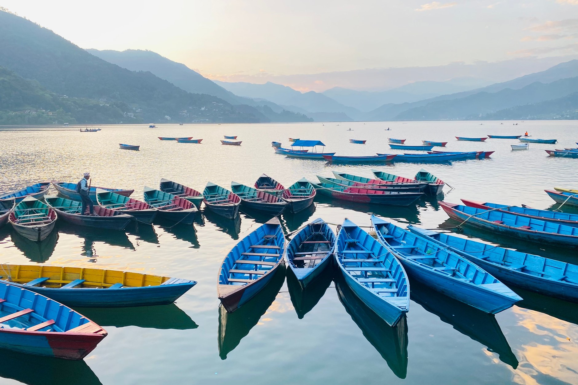 Colorful wooden rowboats moored along the tranquil shoreline of Phewa Lake in Pokhara