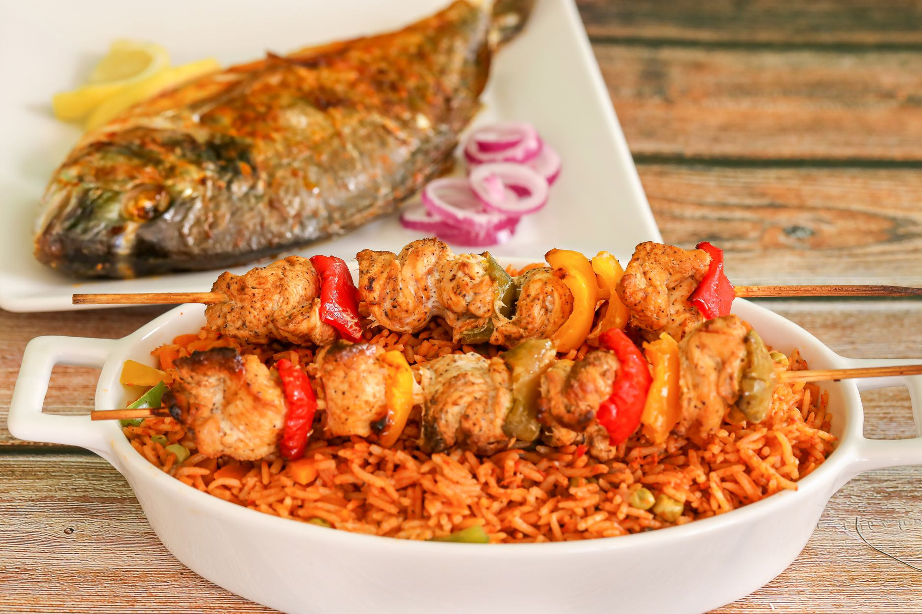 A plate of rich reddish-orange Nigerian jollof rice garnished with seasoned meats, plantains, and peppers