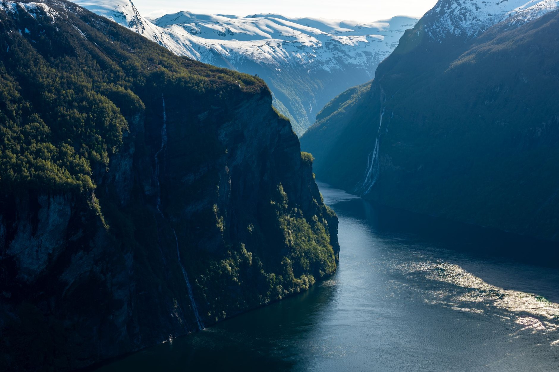 Rushing glacial waterfall cascading into a lush green fjord valley in western Norway