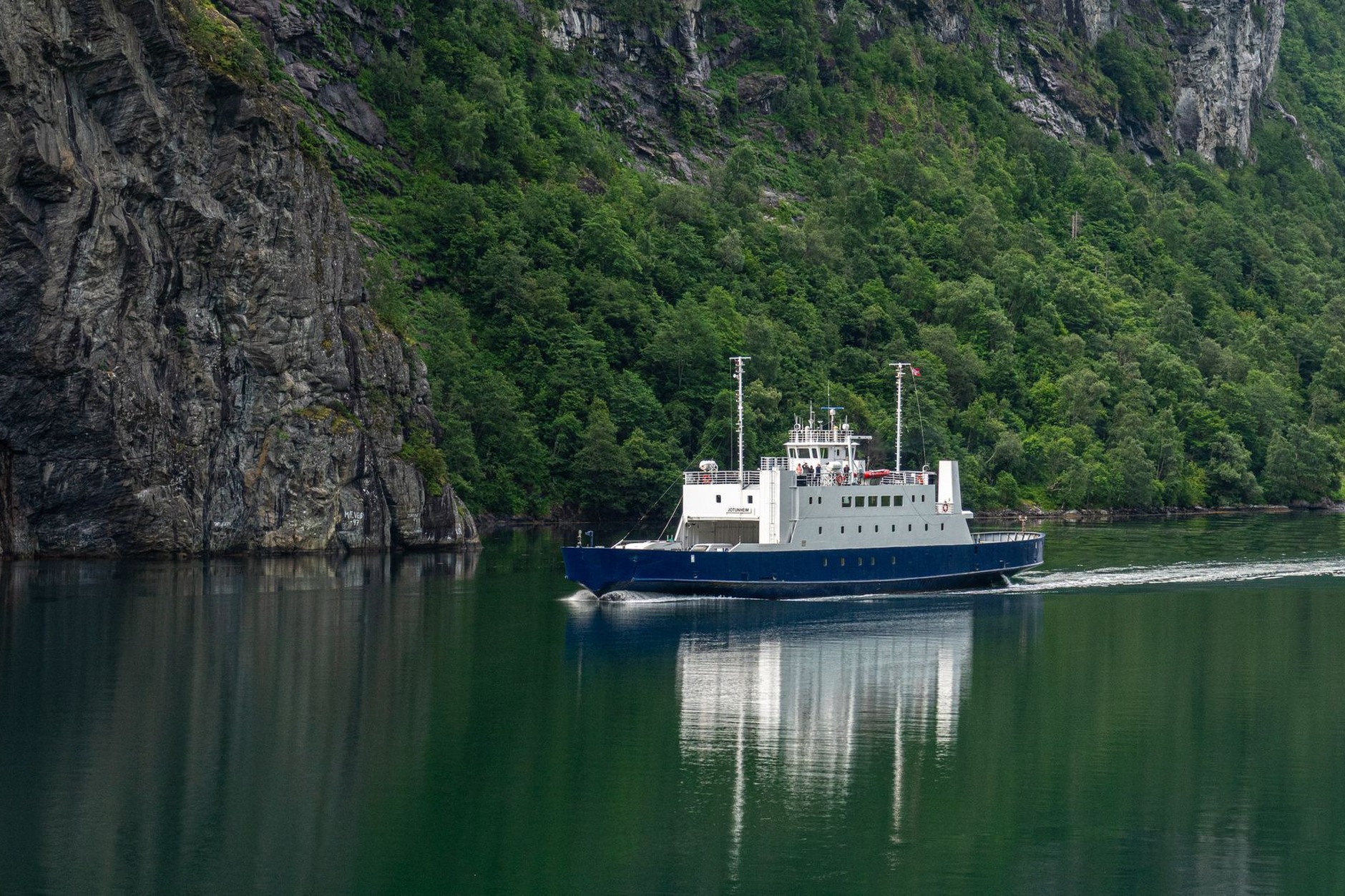 Electric passenger catamaran cruising beneath the towering sheer cliffs of Naeroyfjord