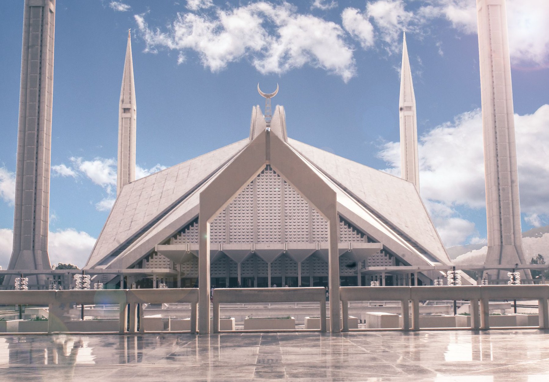Monumental modernist white marble Faisal Mosque with four soaring minarets framed by the green Margalla Hills in Islamabad