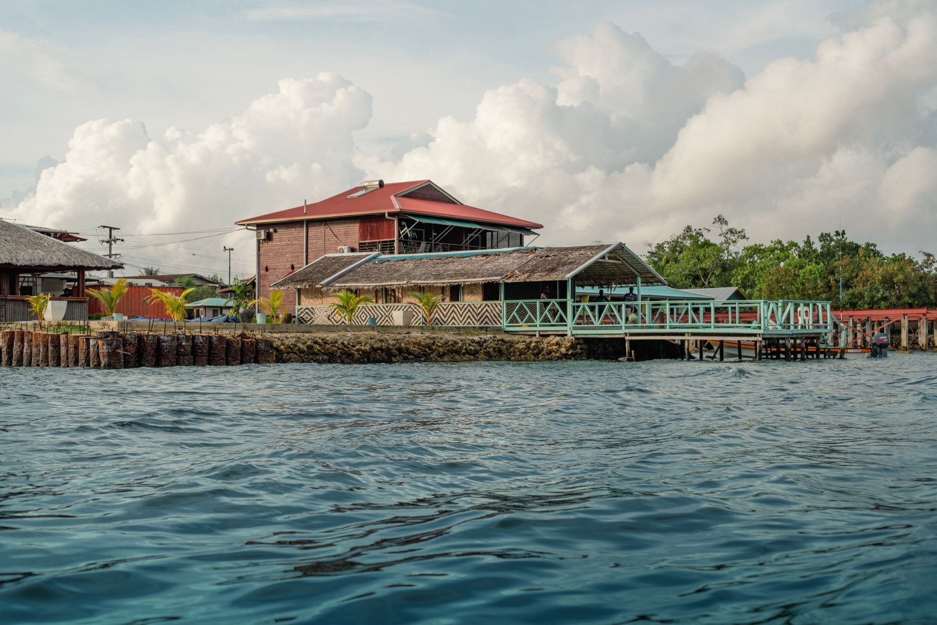 Coastal waterfront lodge and lush tropical rainforest shoreline overlooking turquoise sea waters in Papua New Guinea