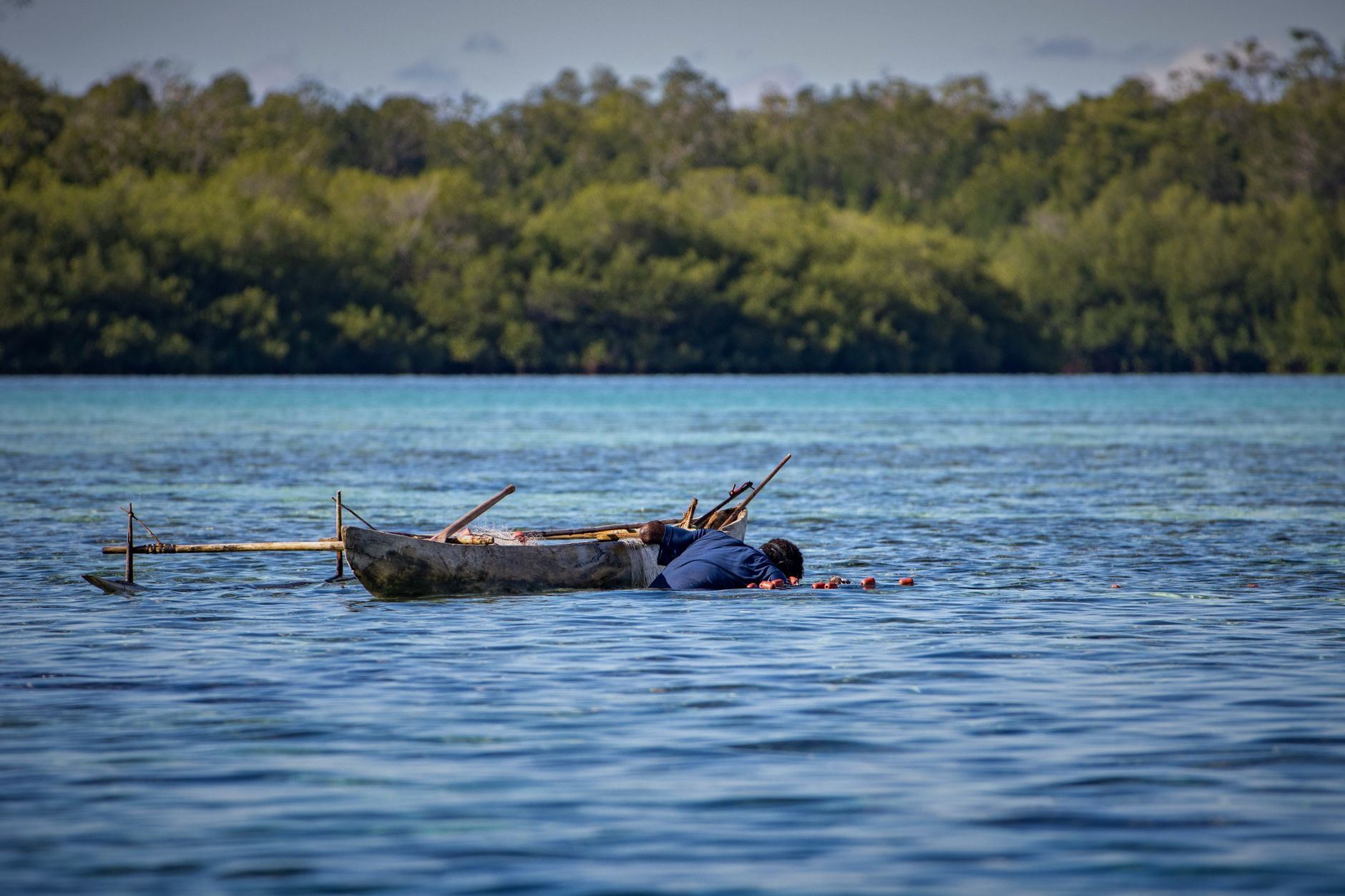 Local fisherman navigating a slender wooden dugout canoe across pristine translucent ocean waters in Papua New Guinea