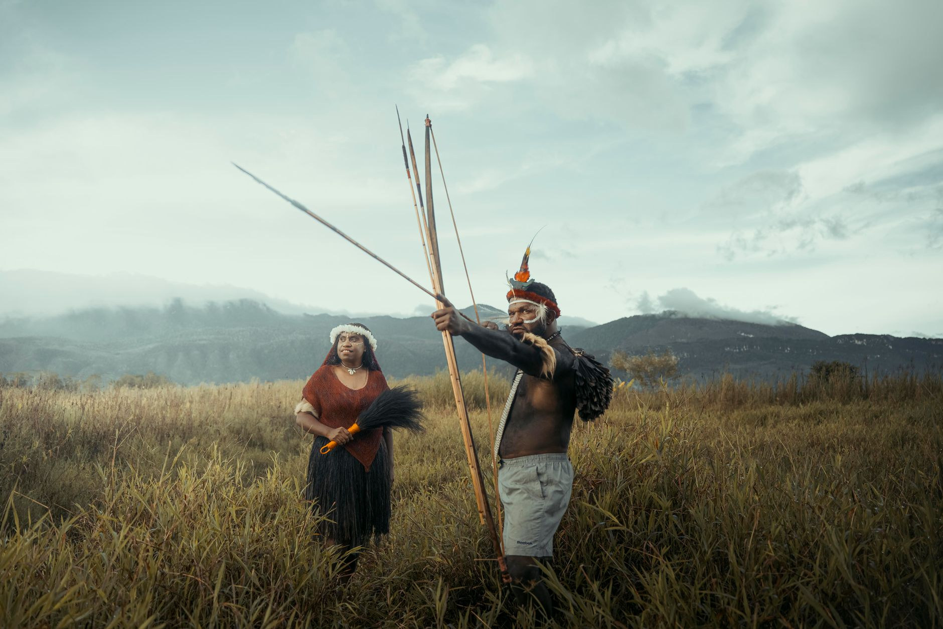 Highlands warriors in traditional ceremonial dress holding spears before lush mountain peaks in Papua New Guinea