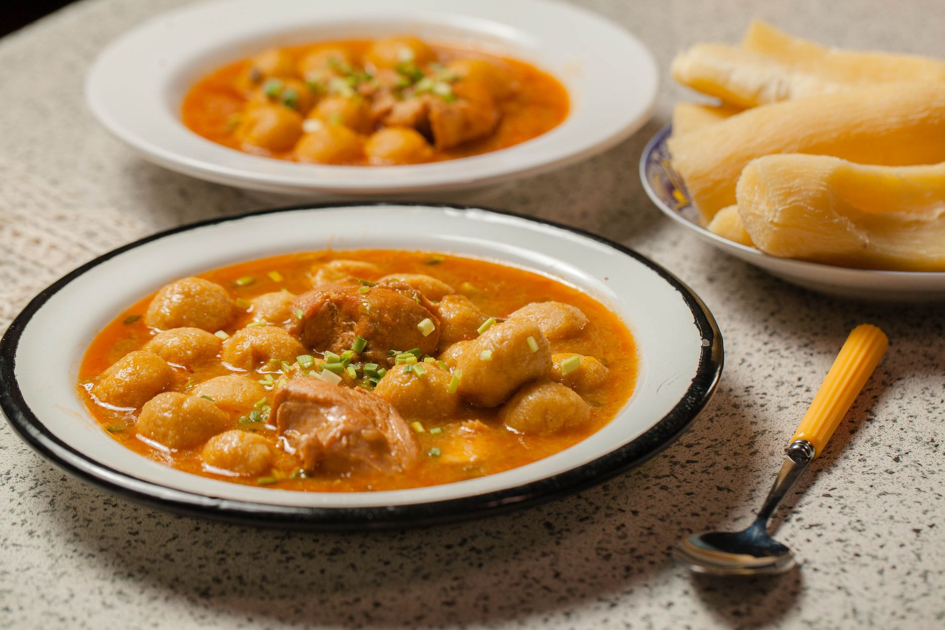 Rustic clay bowl of rich golden chicken broth with small round cornmeal and cheese dumplings garnished with fresh herbs