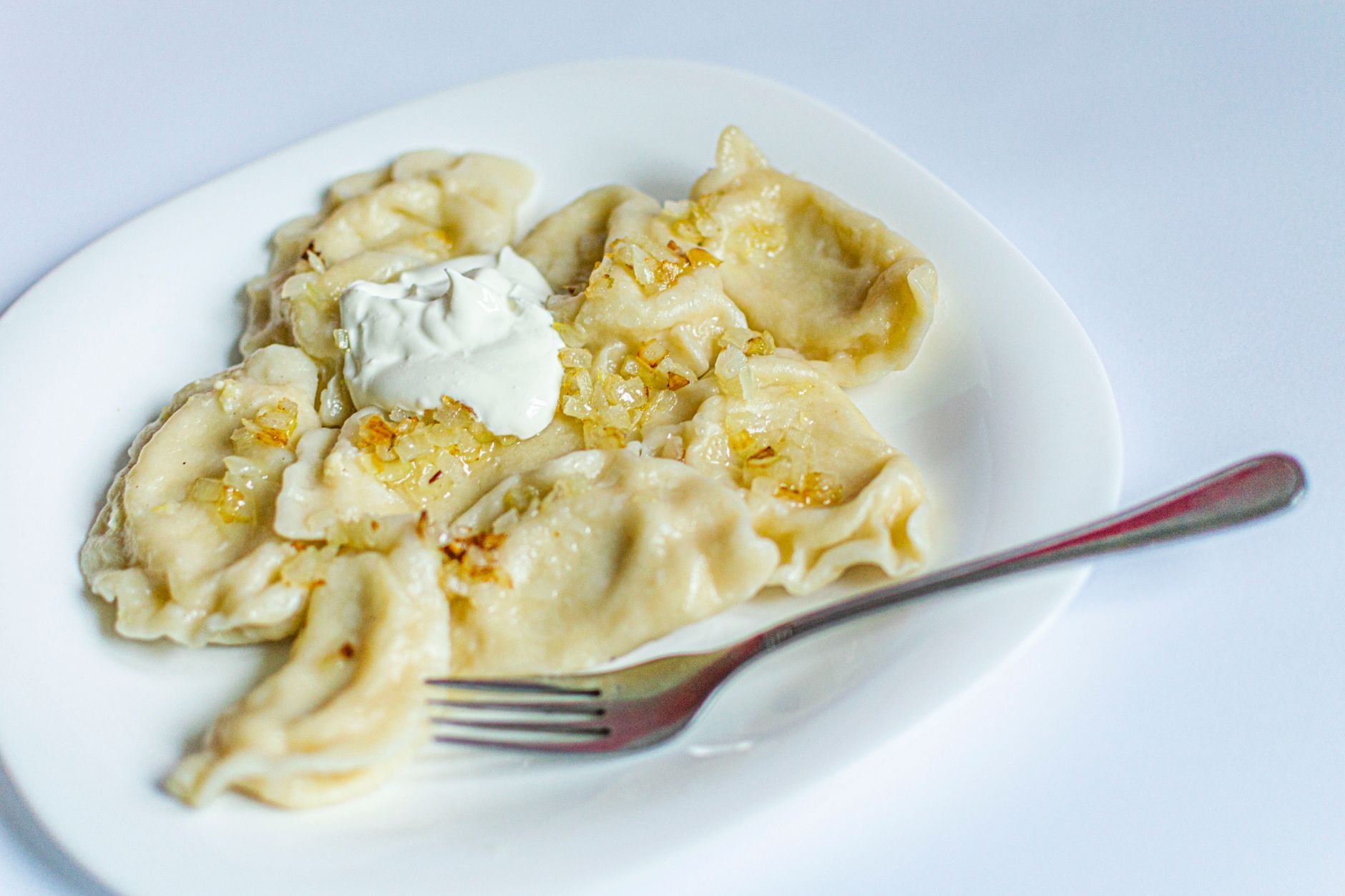 Plate of golden pan-fried Polish pierogi dumplings topped with caramelized onions and fresh herb garnish