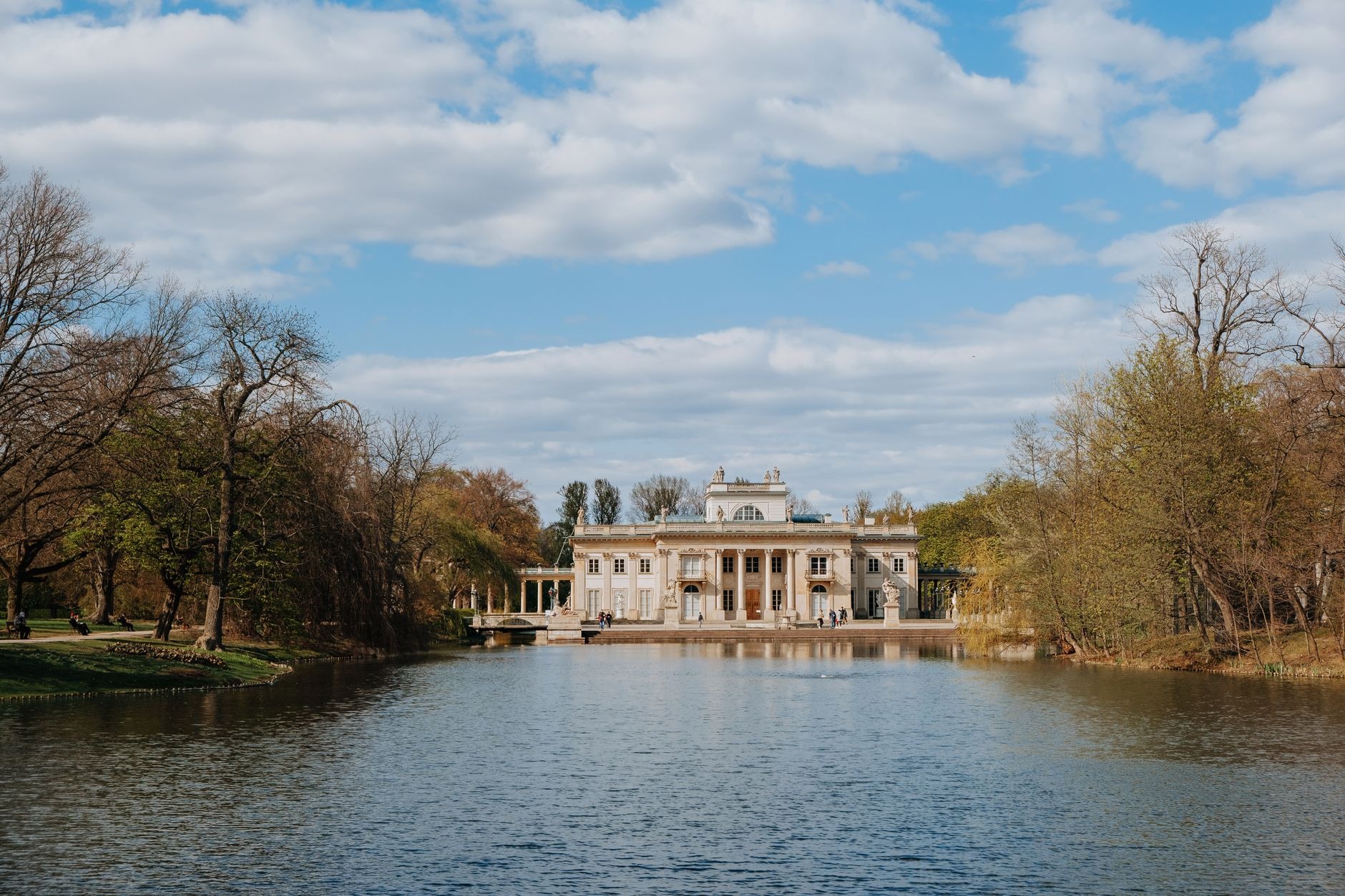 Neoclassical Palace on the Isle reflecting in tranquil park waters surrounded by green trees in Warsaw's Royal Lazienki Park