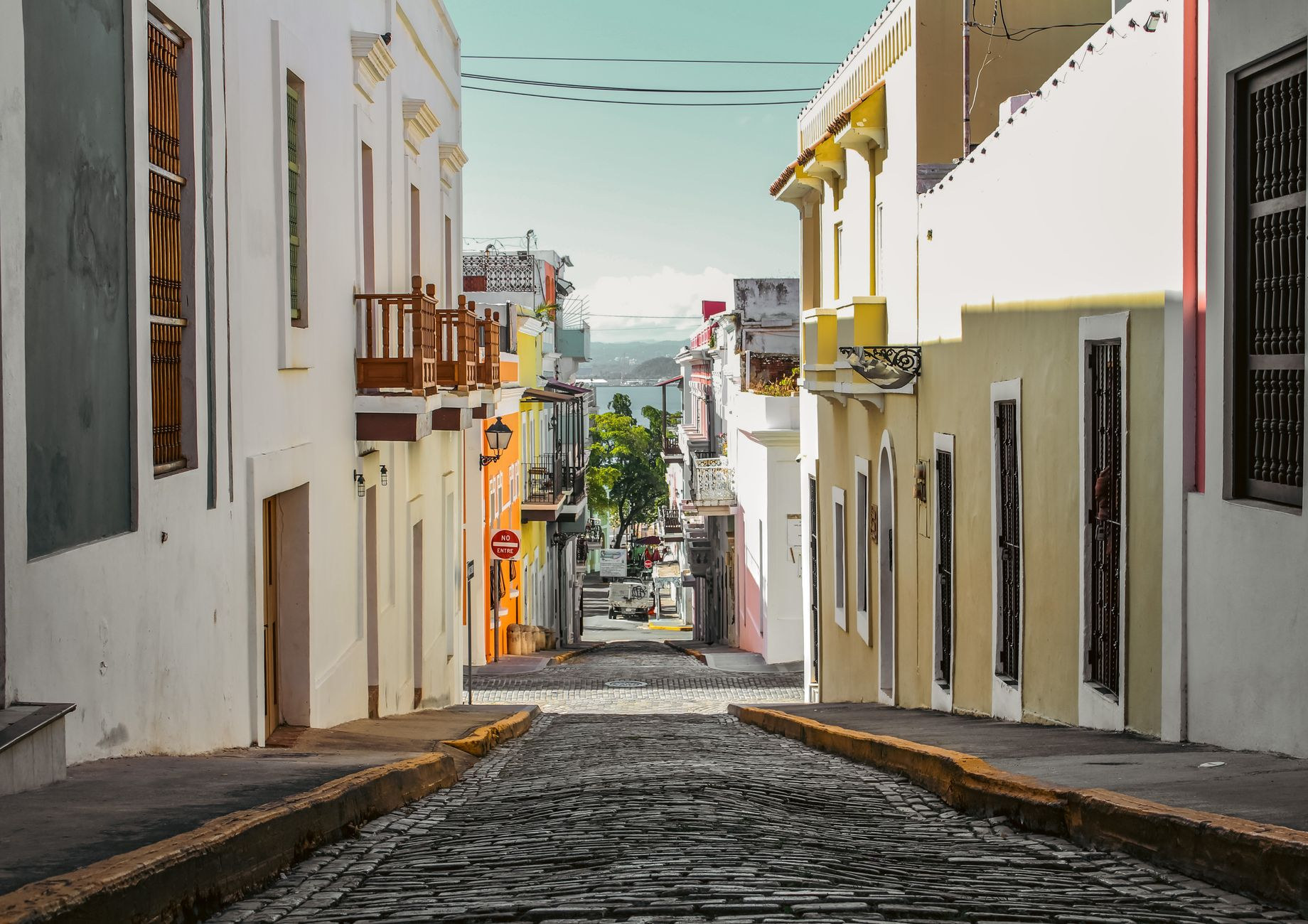 Pastel-painted Spanish colonial townhouses with wrought-iron balconies lining a blue adoquine cobblestone street