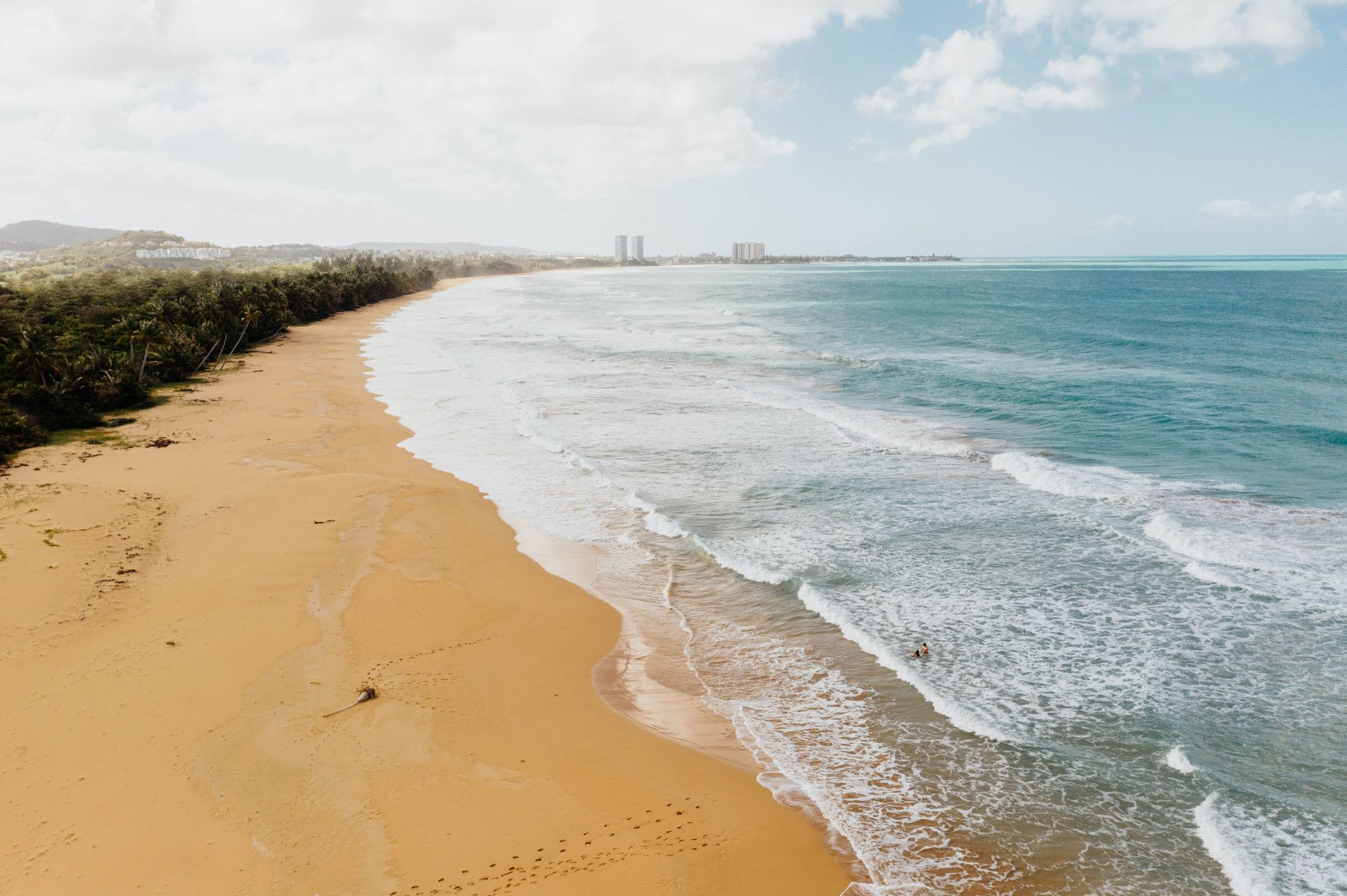 A sweeping golden sand beach with gentle turquoise waves and coconut palm groves along the coast
