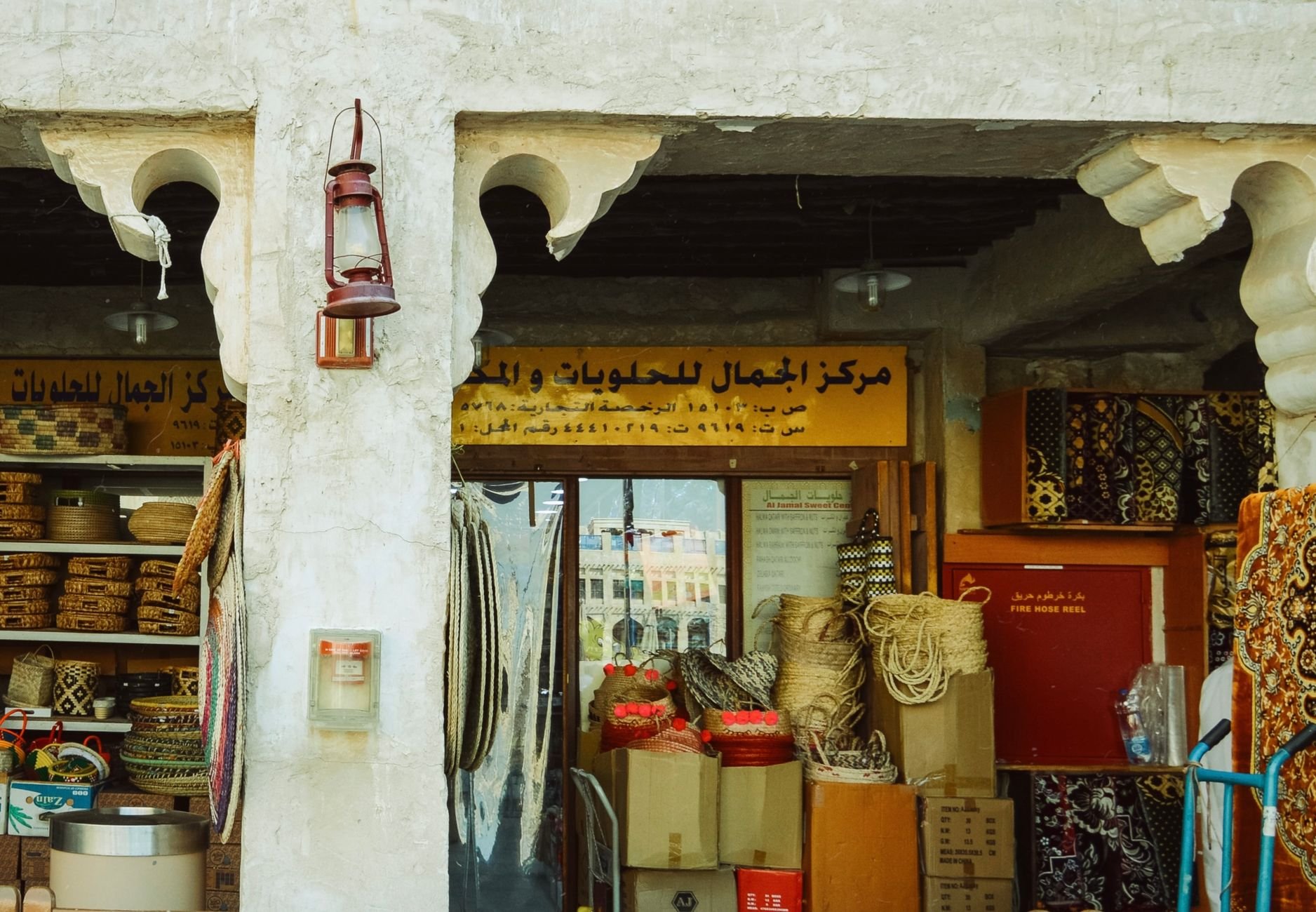Mud-rendered stone alleyways of Souq Waqif bustling in the evening with outdoor diners, glowing brass lanterns, and spice sacks