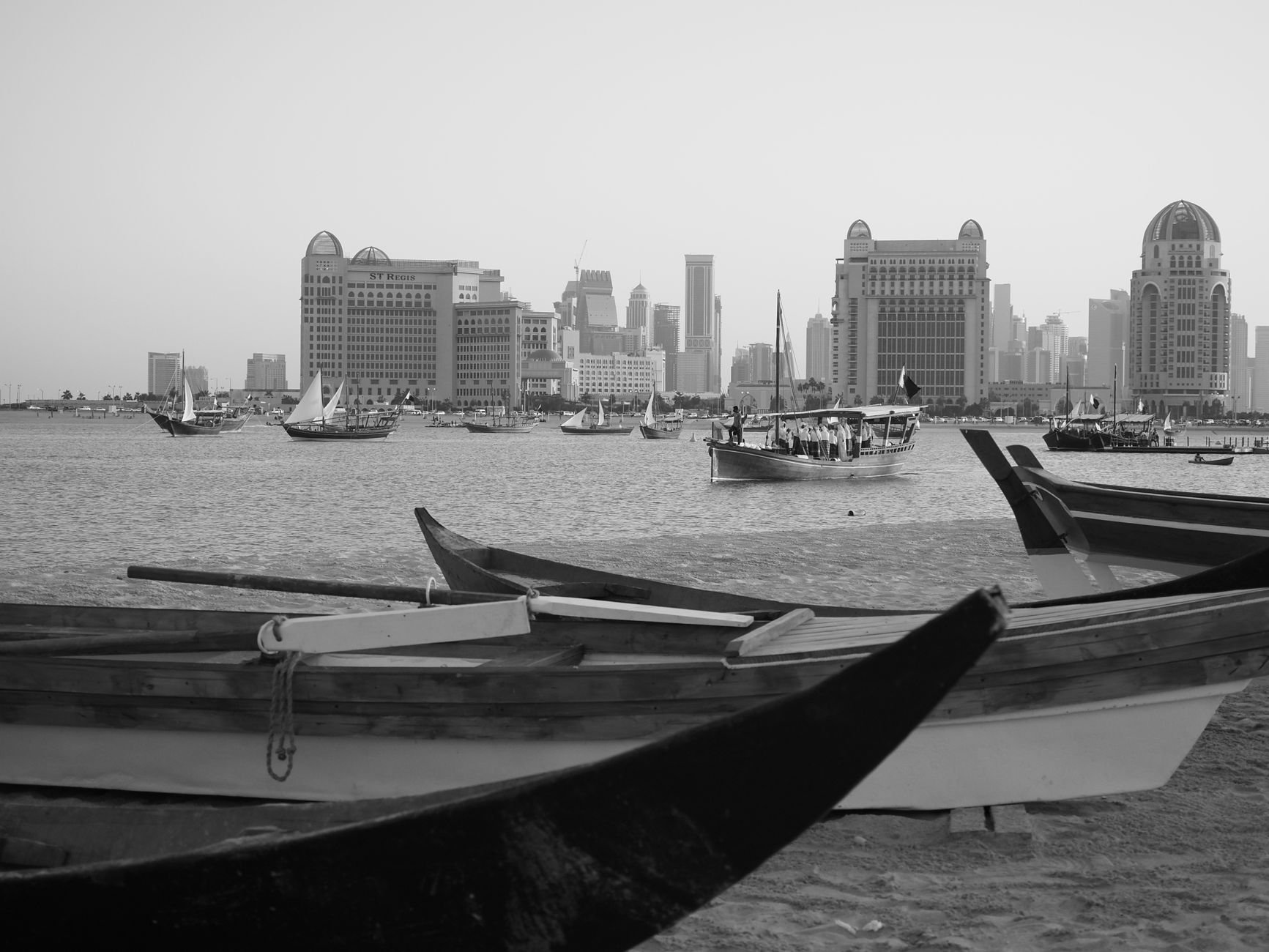 Fleet of traditional wooden Qatari dhow fishing and pearling boats moored in Doha harbor with modern West Bay towers behind