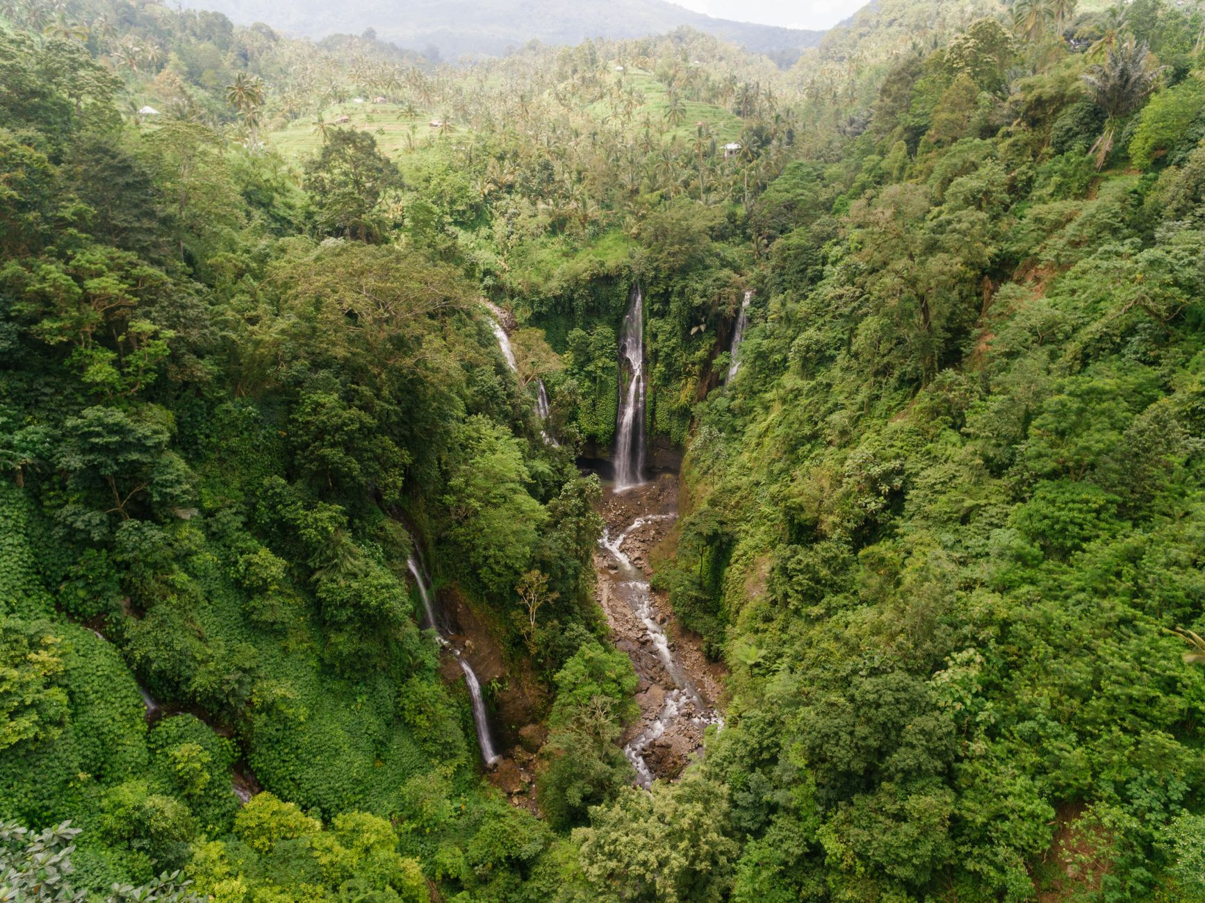 Multiple streams of clean freshwater cascading over lush green volcanic cliffs into a deep natural pool