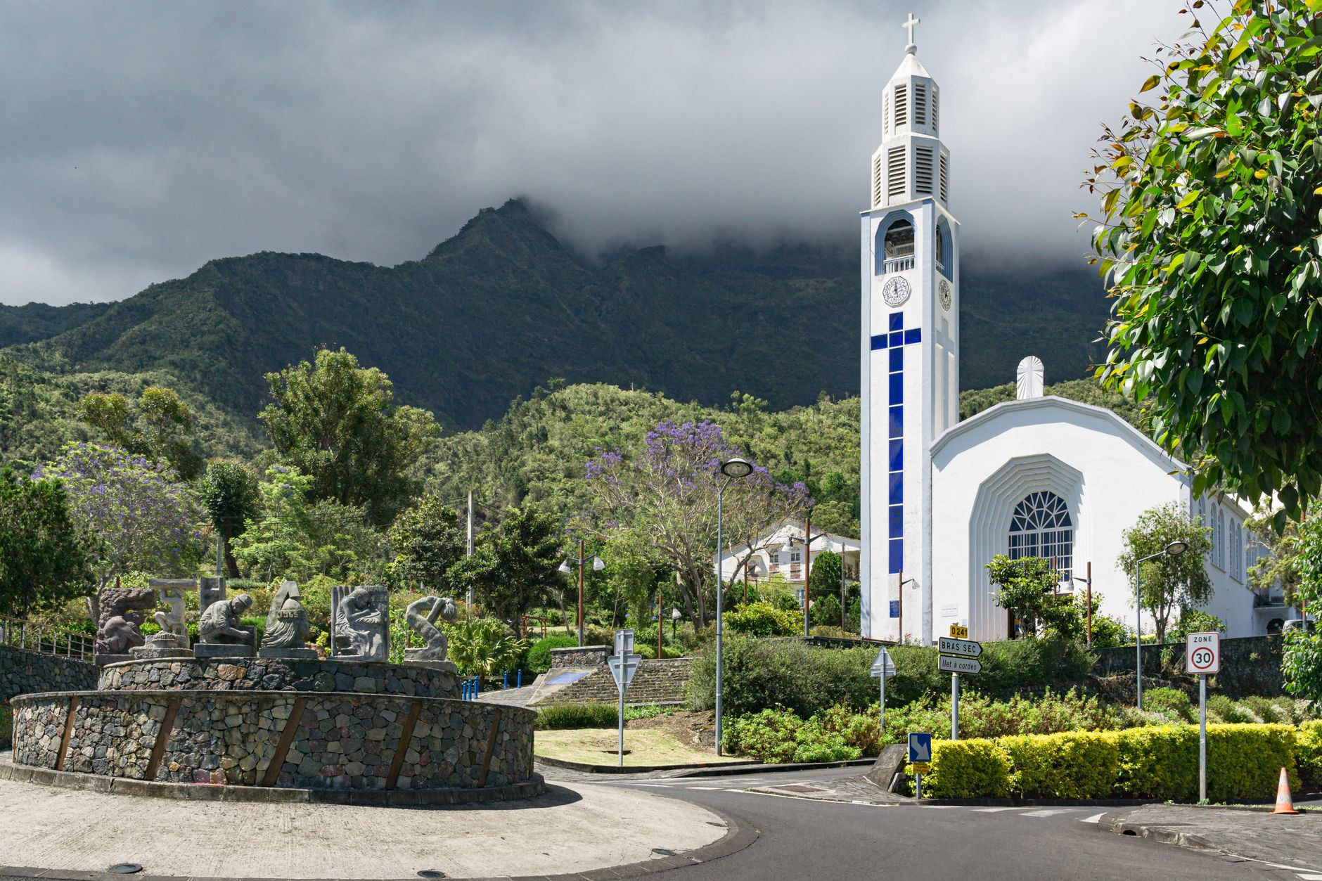 The iconic white bell tower of Notre-Dame-des-Neiges church framed by sheer volcanic peaks in the mountain town of Cilaos