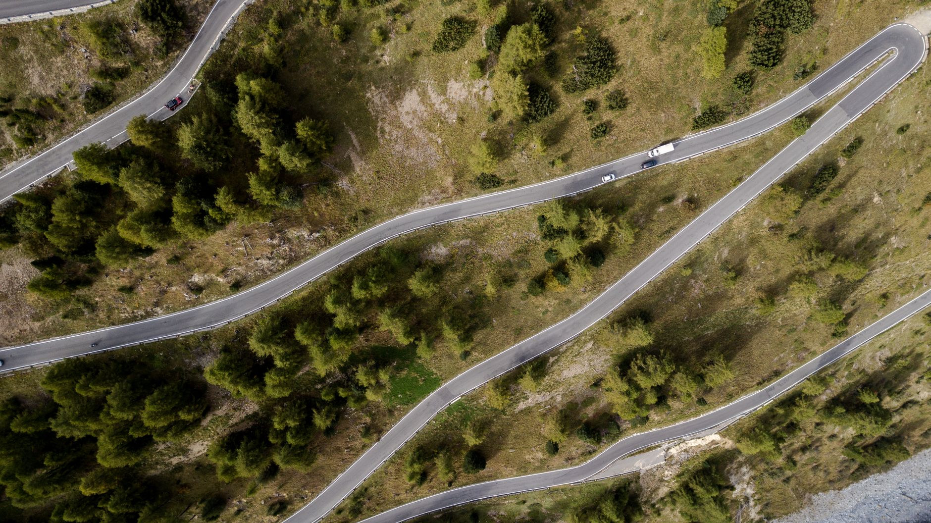 Aerial view of a winding asphalt mountain highway with sharp hairpin turns cutting through dense forest slopes