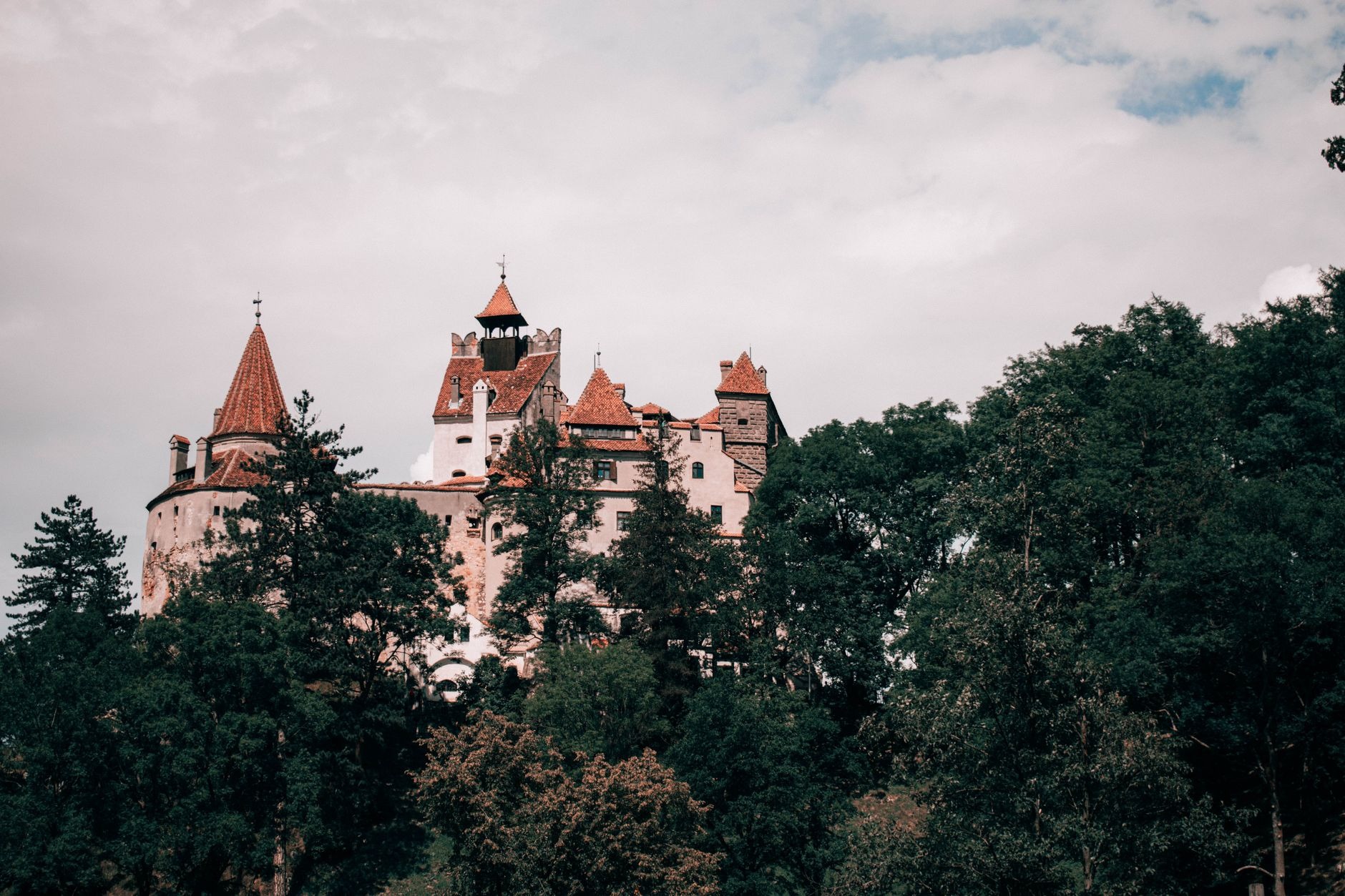 Dramatic Gothic stone watchtowers and red roofed ramparts of Bran Castle perched atop a steep rocky promontory