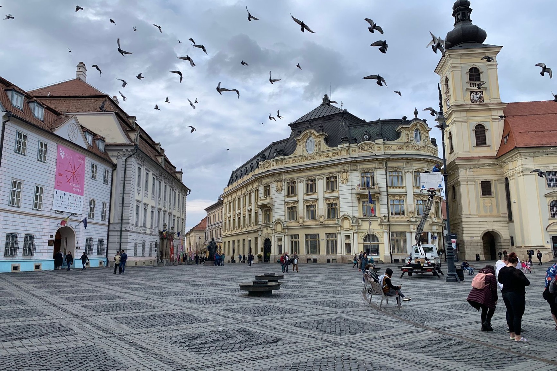 Expansive cobblestone expanse of Sibiu's Grand Square featuring historic pastel baroque facades with iconic roof eye windows