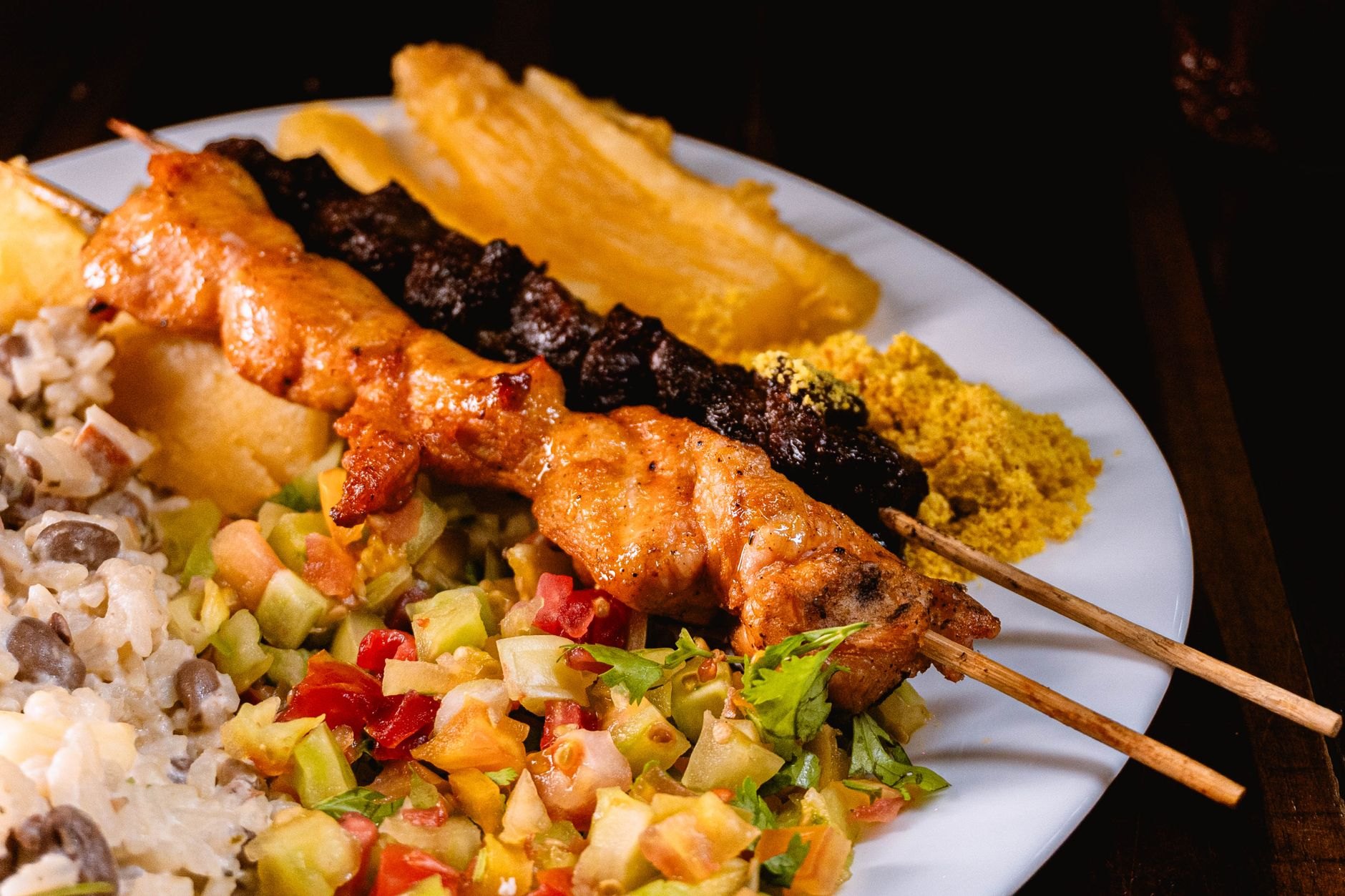 Wooden skewers of grilled goat brochettes served with roasted plantains (aloko) and spicy piri-piri sauce