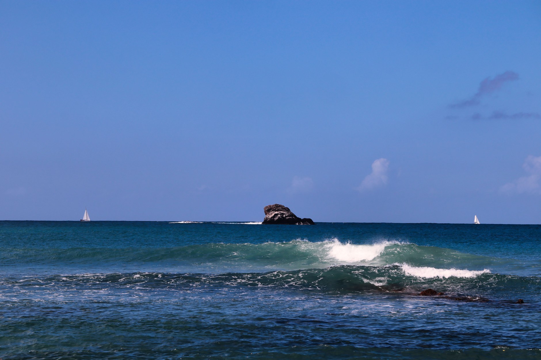 Ocean seascape with sailboats and waves washing against the rocky shoreline in northern Saint Lucia