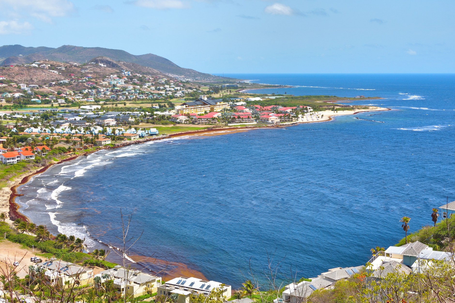Aerial view of a sweeping crescent sand beach and calm turquoise ocean bay with tropical greenery