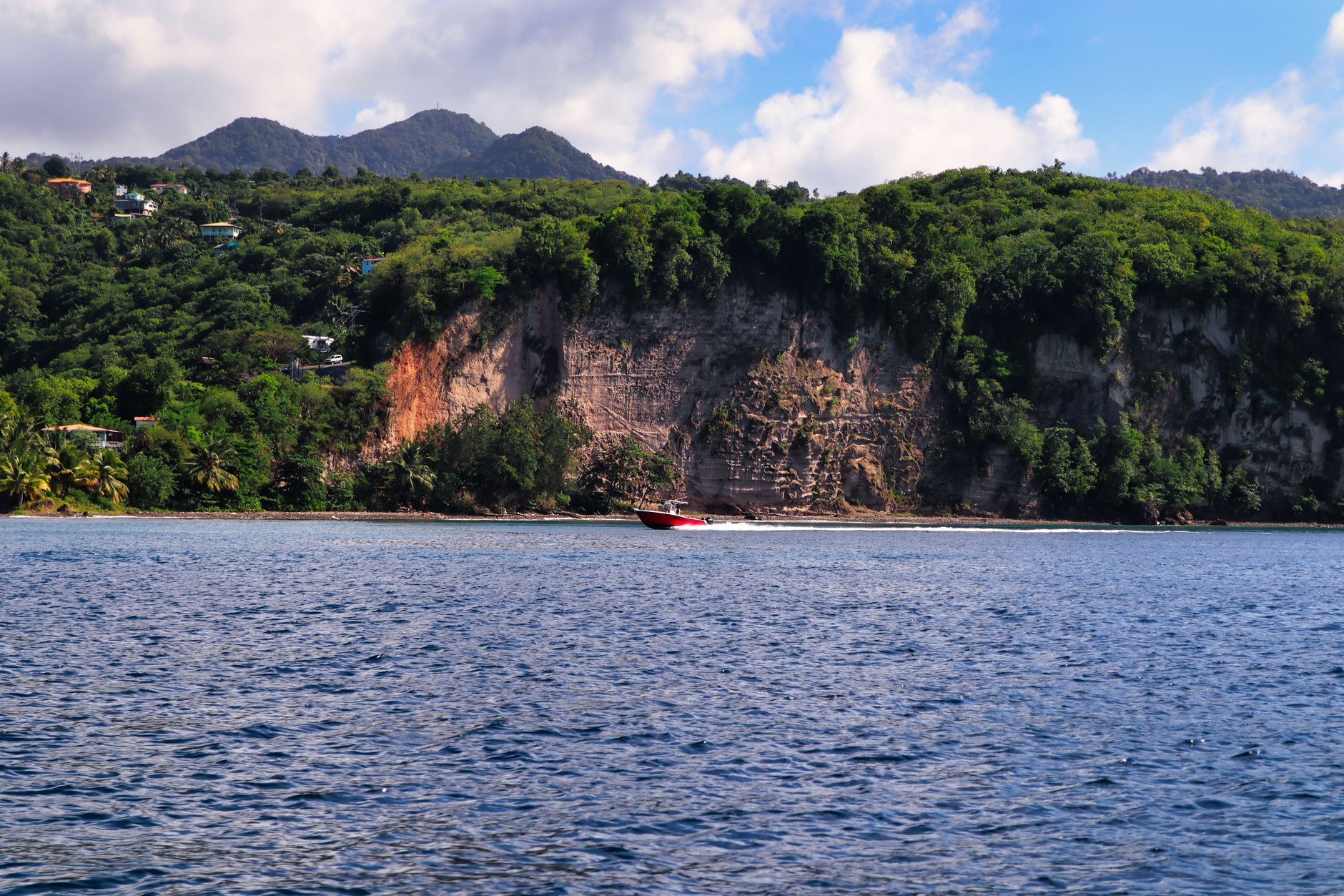 Speedboat cruising along the steep green cliffs and shoreline of Saint Lucia on clear blue waters