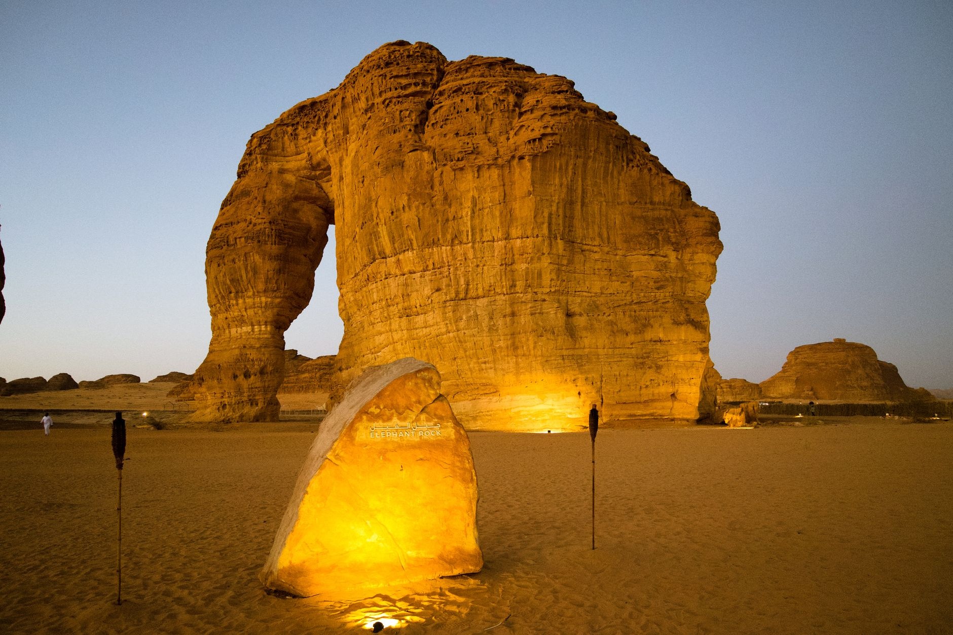 Colossal natural sandstone formation of Elephant Rock glowing deep crimson under an evening desert sunset in AlUla