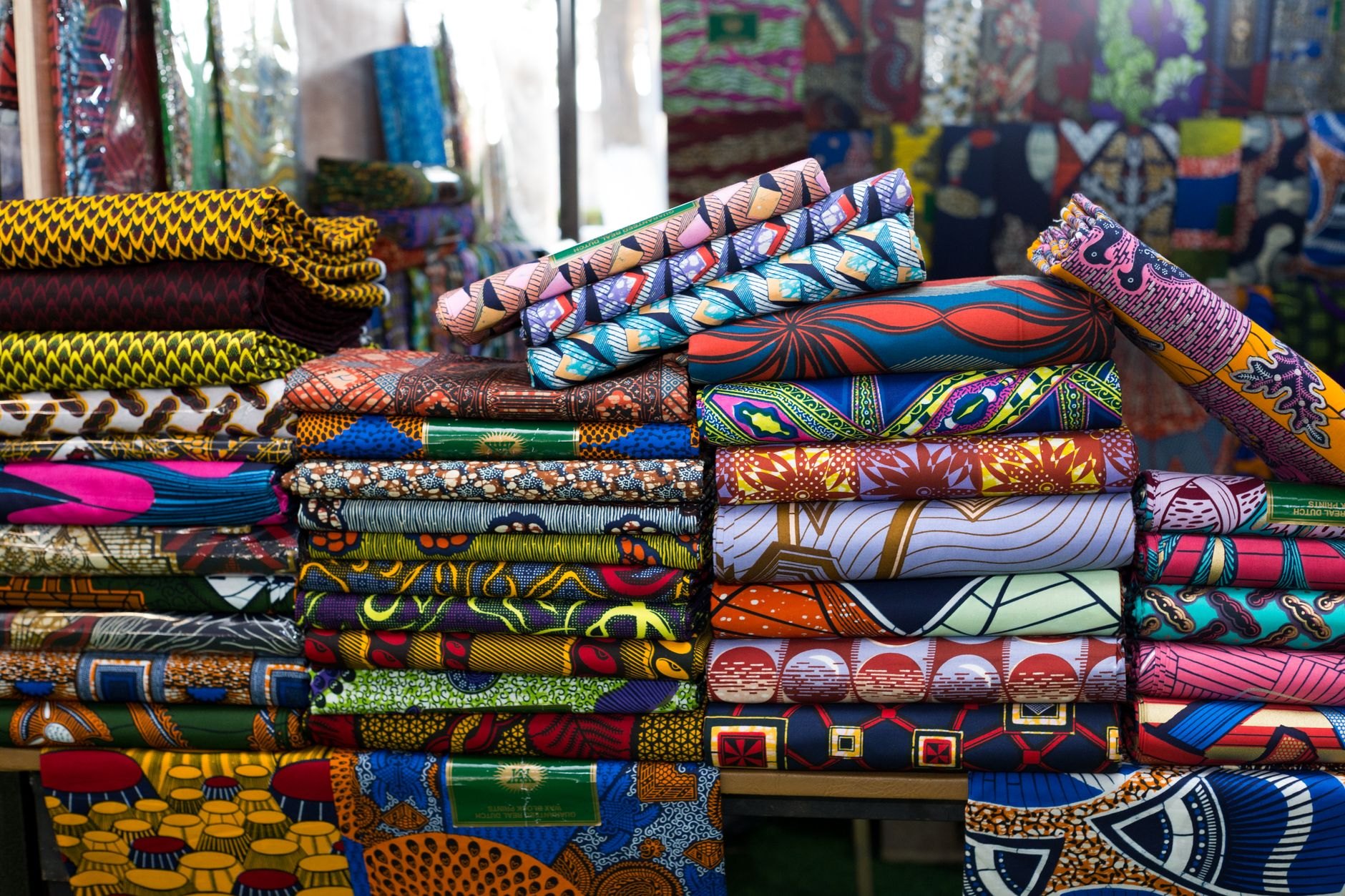 Stalls draped in geometric wax-print cotton fabrics and woven bazin textiles inside a bustling Dakar market