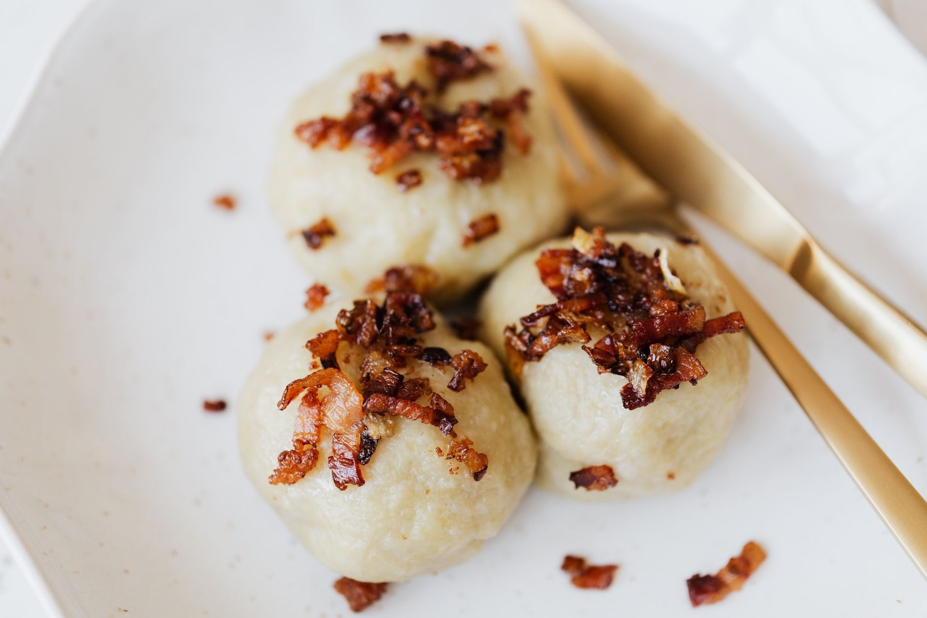 Steaming bowl of traditional potato dumplings smothered in creamy sheep milk bryndza cheese and topped with crispy smoked bacon bits