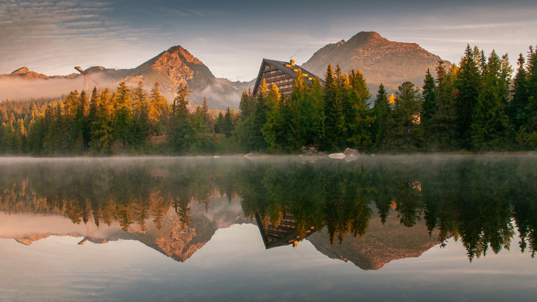Glassy alpine reflection of jagged granite High Tatras peaks on the surface of Štrbské Pleso glacial lake fringed with pine trees