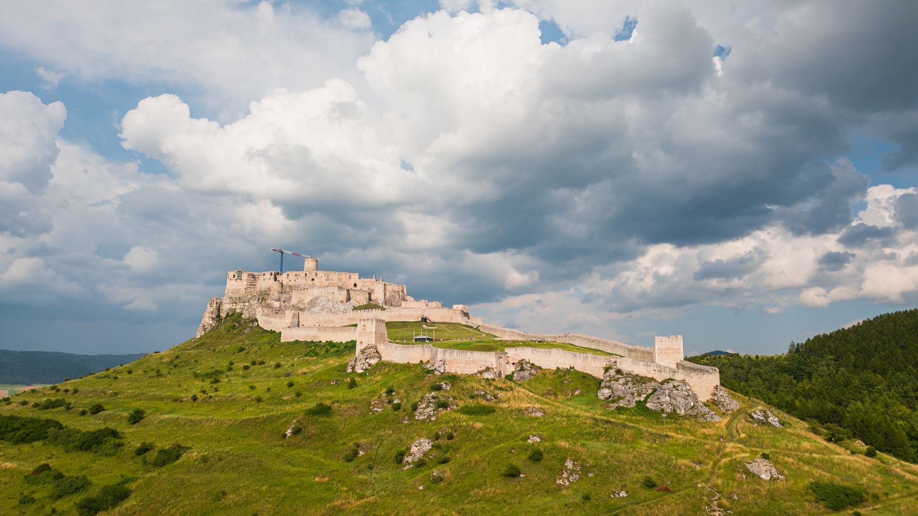 Massive sprawling white limestone fortifications of Spiš Castle dominating a high grassy travertine hill under dramatic skies