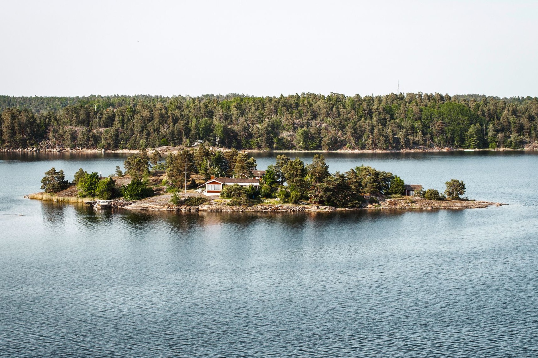 A passenger ferry navigating past granite islets and red wooden summer cottages in the Stockholm archipelago