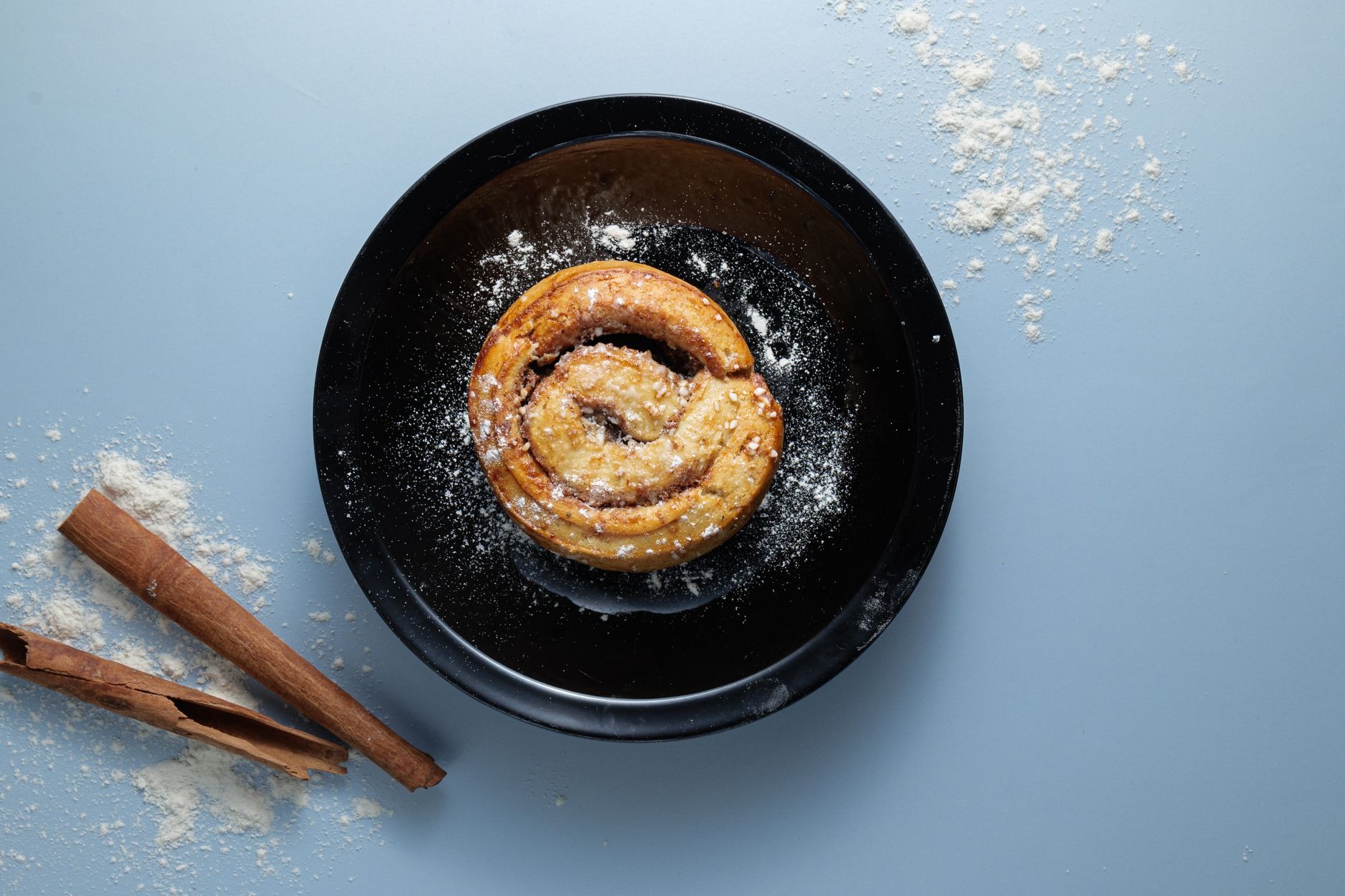 Freshly baked Swedish cardamom and cinnamon bun kanelbulle dusted with pearl sugar beside a cup of black filter coffee