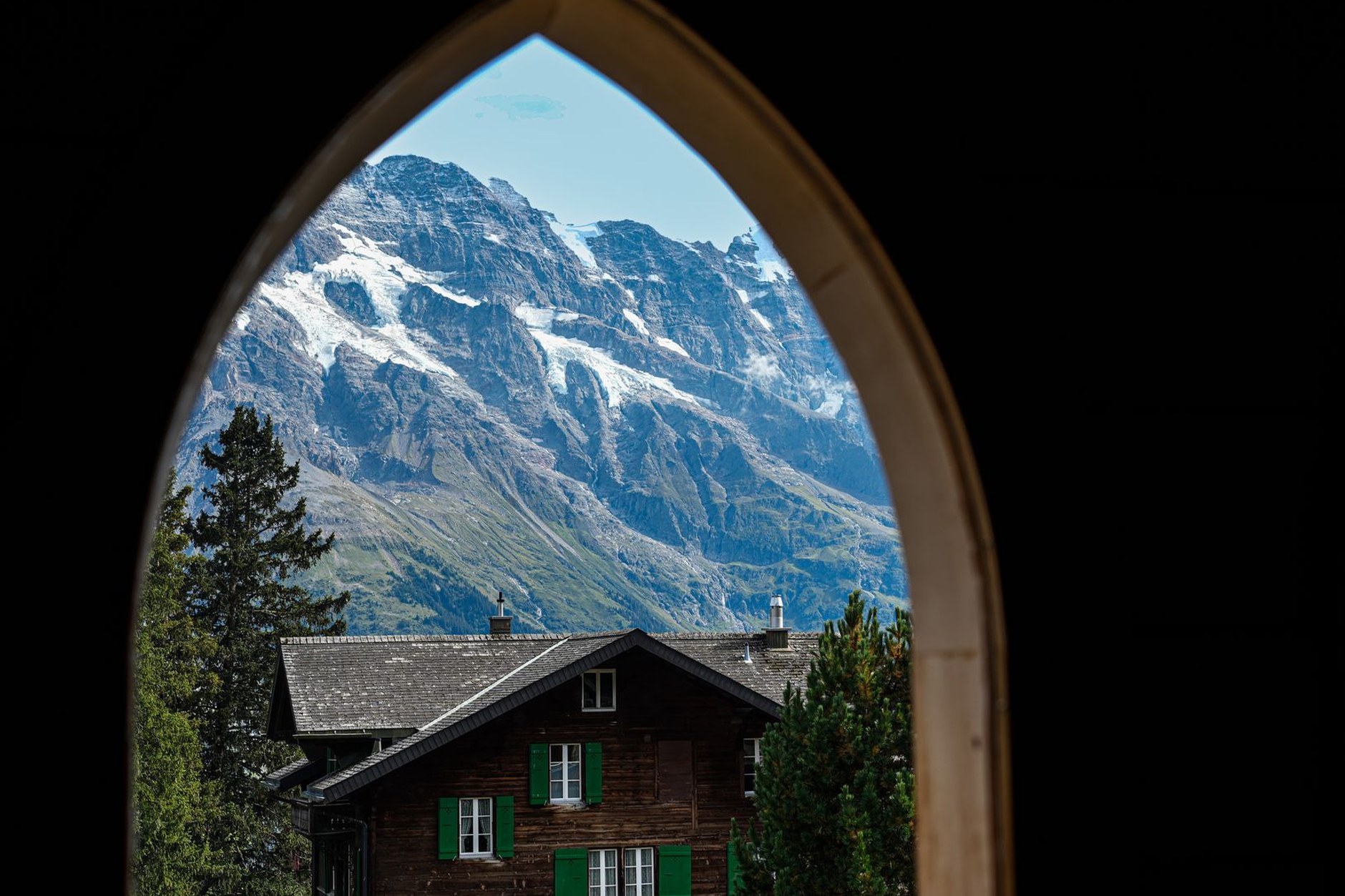 Hikers traversing a wildflower-strewn alpine trail past traditional timber barns in the Bernese Alps
