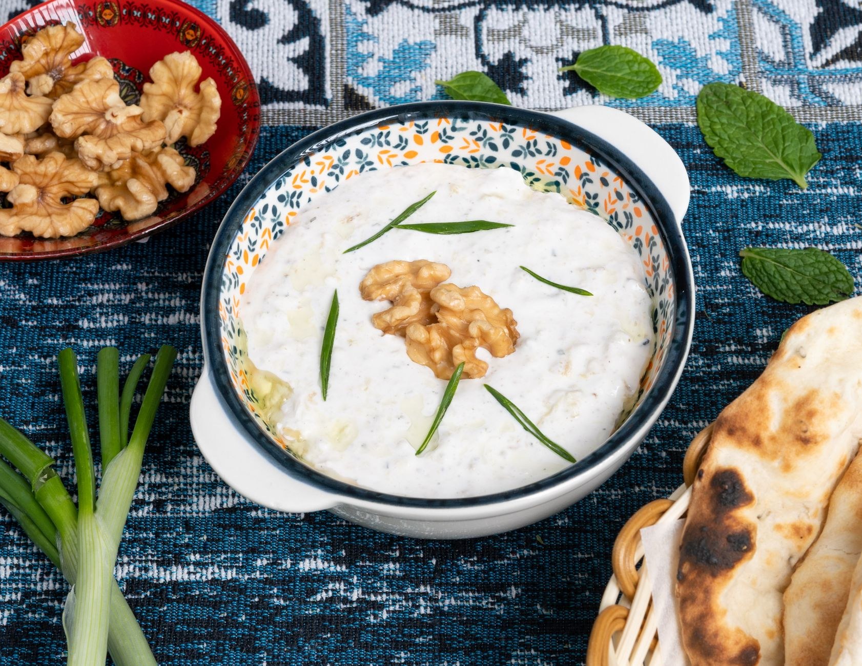 Traditional Tajik qurutob in a carved wooden bowl with torn flatbread, savory yogurt sauce, and caramelized onions