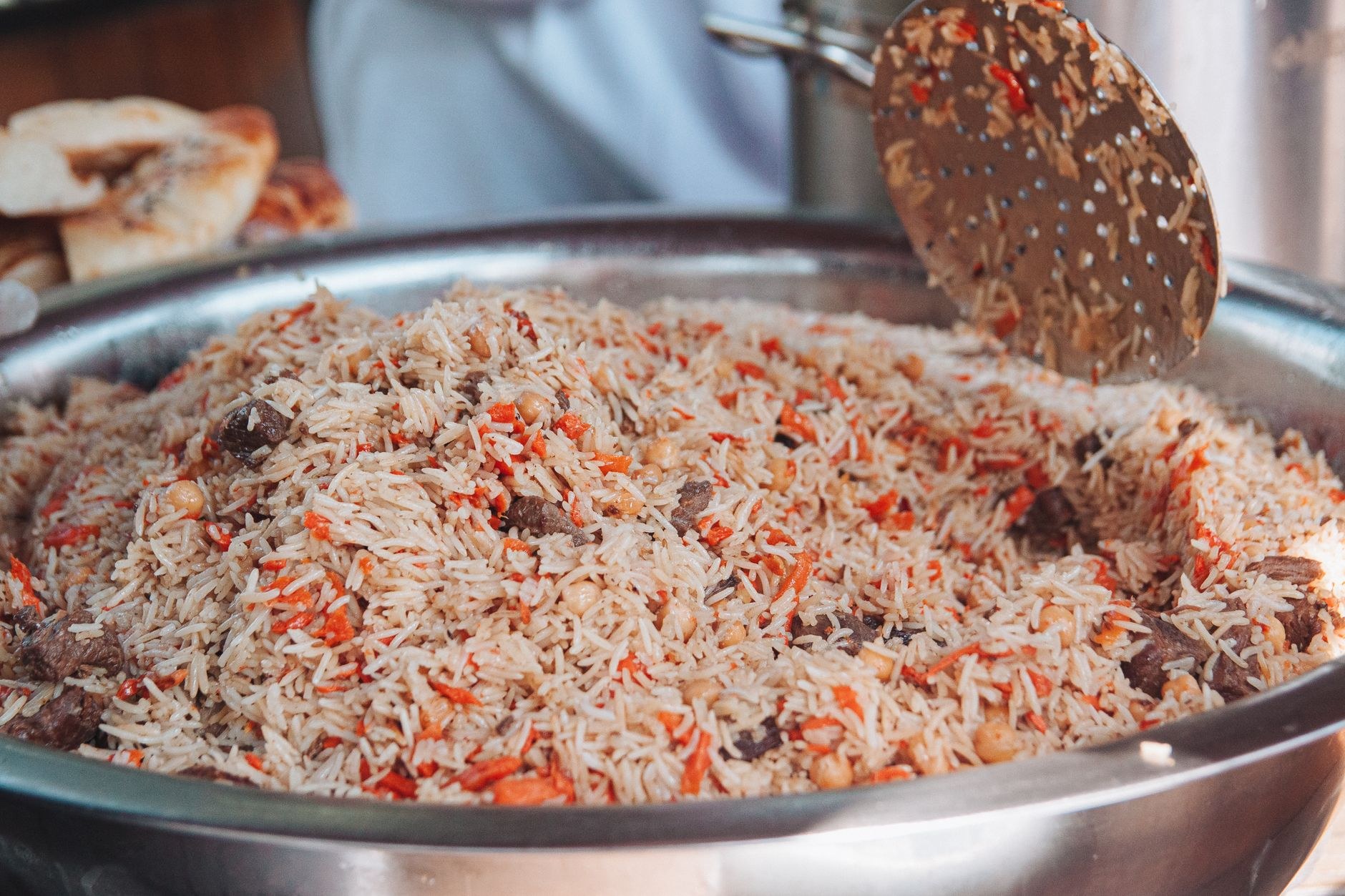 A steaming platter of traditional Tajik plov featuring tender lamb, yellow carrots, and chickpeas