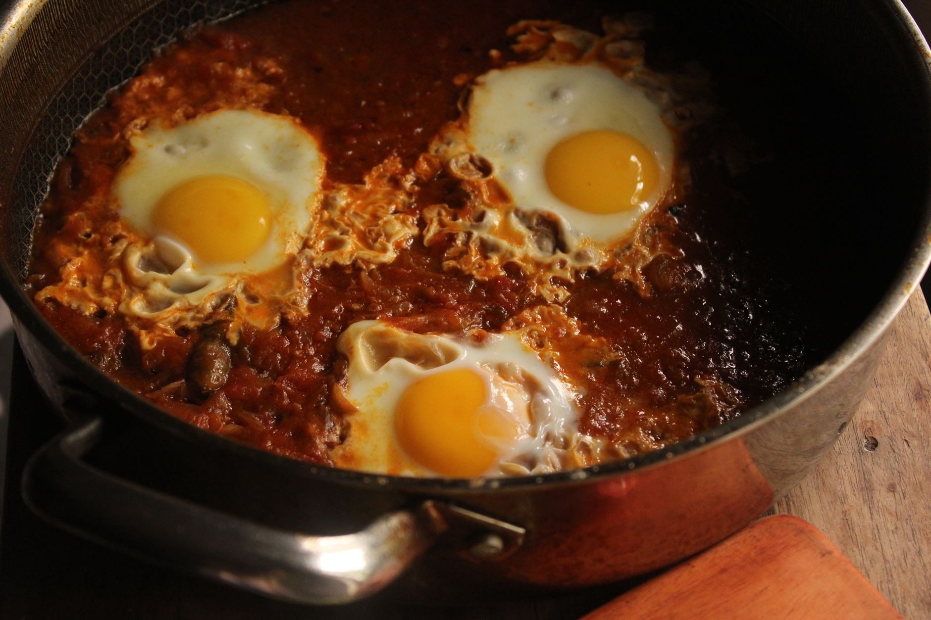 Rich North African shakshuka simmered with tomatoes, red peppers, spicy harissa, and gently poached eggs in a cast-iron skillet