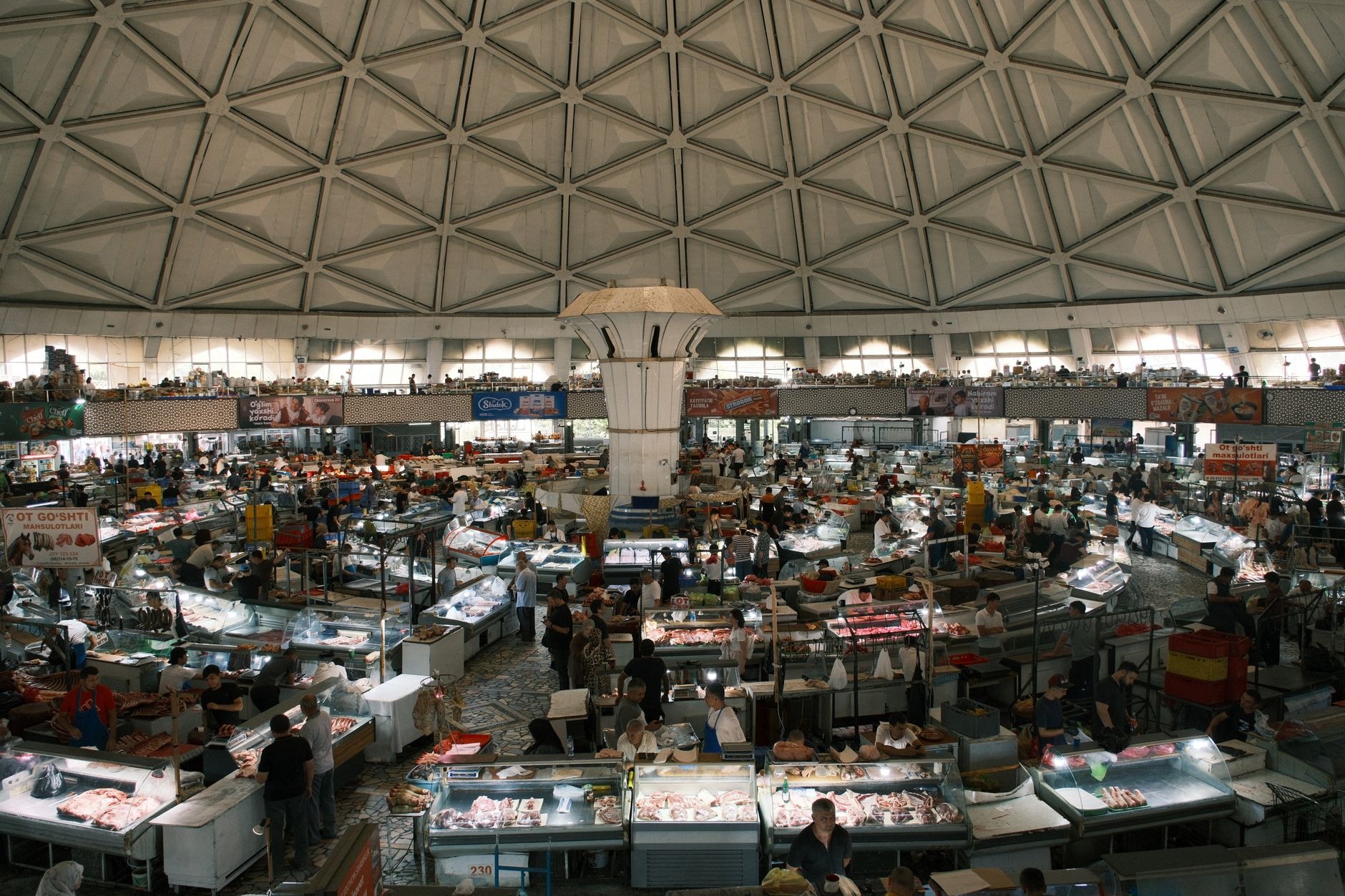 Soaring blue-tiled brutalist dome interior of Chorsu Bazaar in Tashkent filled with multi-tier food stalls and spice pyramids