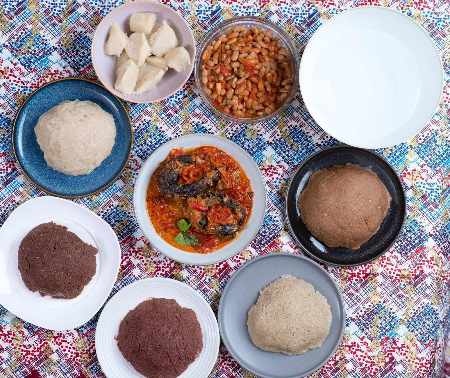 Steaming portions of white maize nshima served with braised pumpkin leaves, village chicken stew, and savory tomato relish