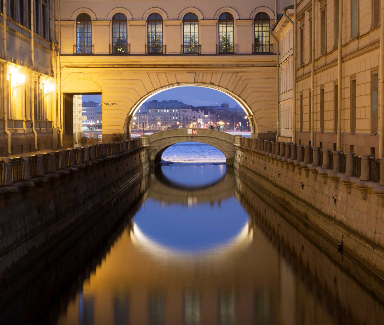 Arched stone bridge and neoclassical pastel facades reflecting in a quiet canal in Saint Petersburg