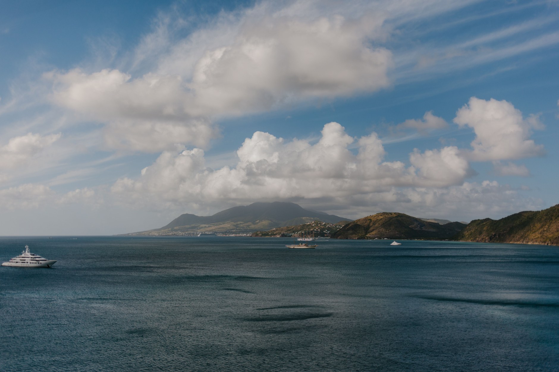 Sheltered turquoise bay framed by green volcanic hills with boats anchored in calm waters