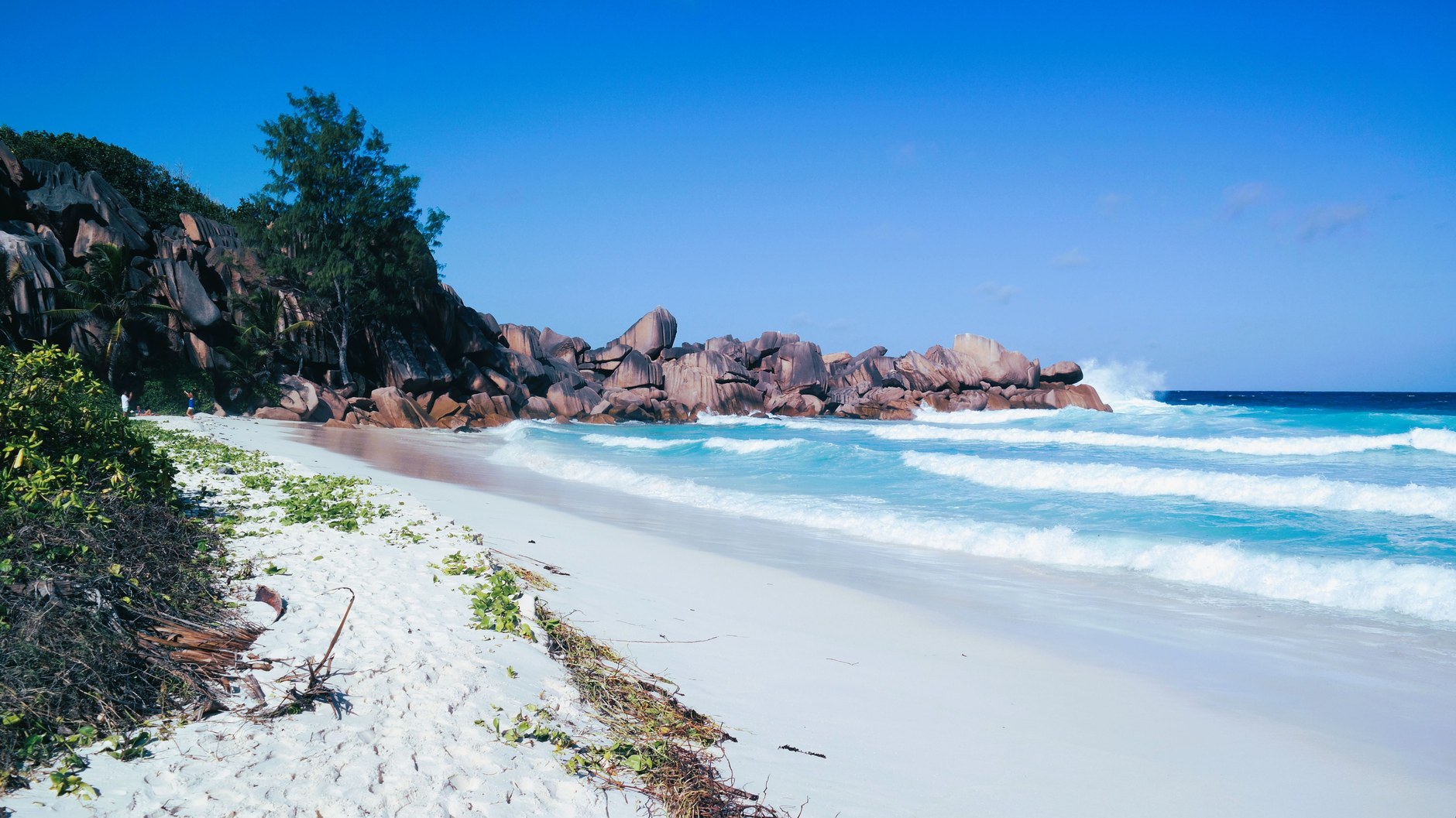Pristine white sand and turquoise ocean waves washing over granite rocks at Anse Lazio in Praslin
